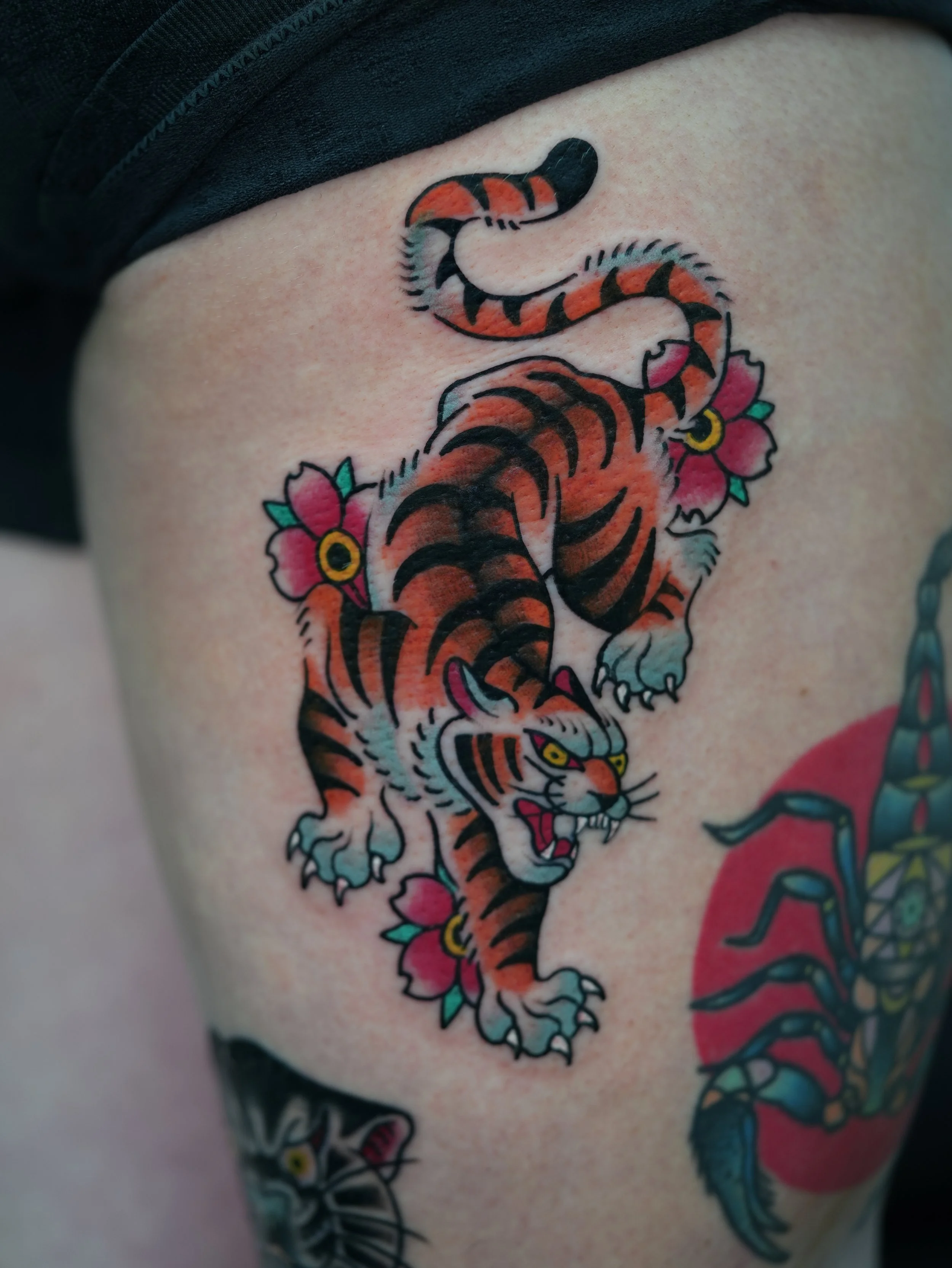 Traditional tiger tattoo featuring bold colors, dynamic movement, and floral details. Custom tattoo by Yonathan Suarez, a traditional and illustrative tattoo artist in West Palm Beach, Florida.