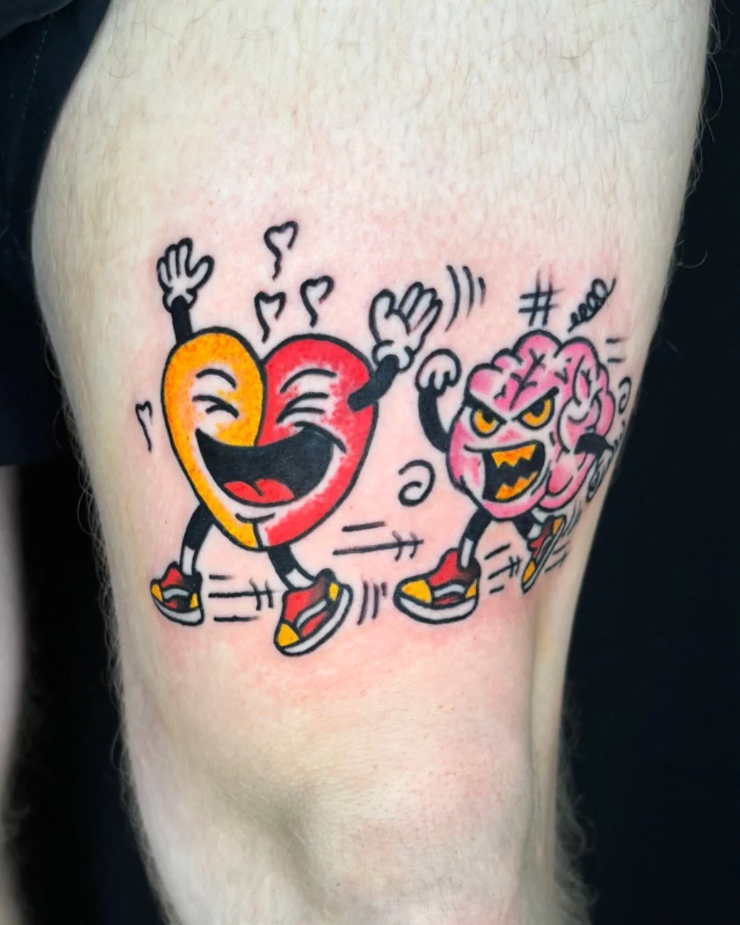 American traditional cartoon tattoo done in West Palm Beach, Florida. This custom tattoo features a playful heart and brain design with expressive faces, bold outlines, strong contrast, and vibrant colors true to classic American traditional tattoo s
