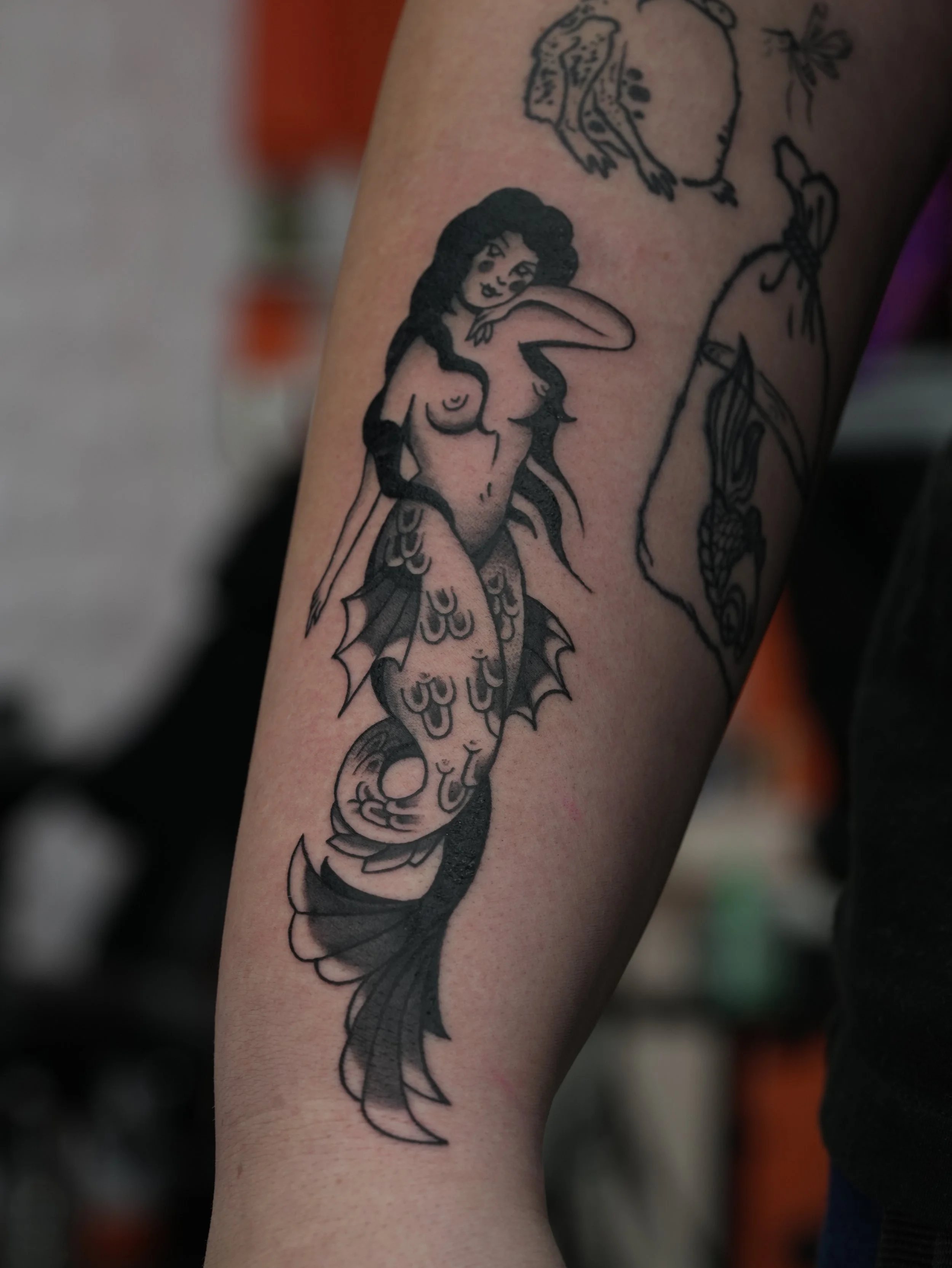 Custom traditional mermaid tattoo in black and grey, featuring flowing hair, detailed scales, and bold linework. Tattooed by Yonathan Suarez, a traditional and illustrative tattoo artist in West Palm Beach, Florida.