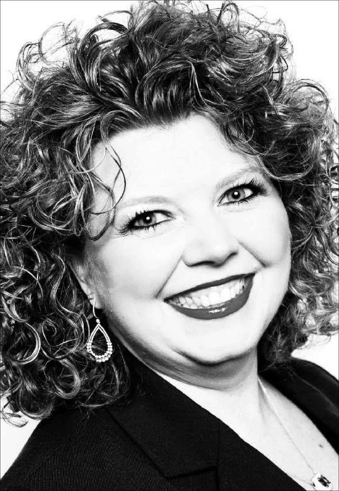 Black and white portrait of a woman with curly hair, smiling and wearing earrings and a necklace