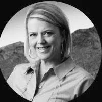 Black and white photo of a woman smiling outdoors with a landscape in the background.