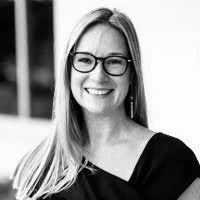 A smiling woman with long hair, wearing glasses and a black top.