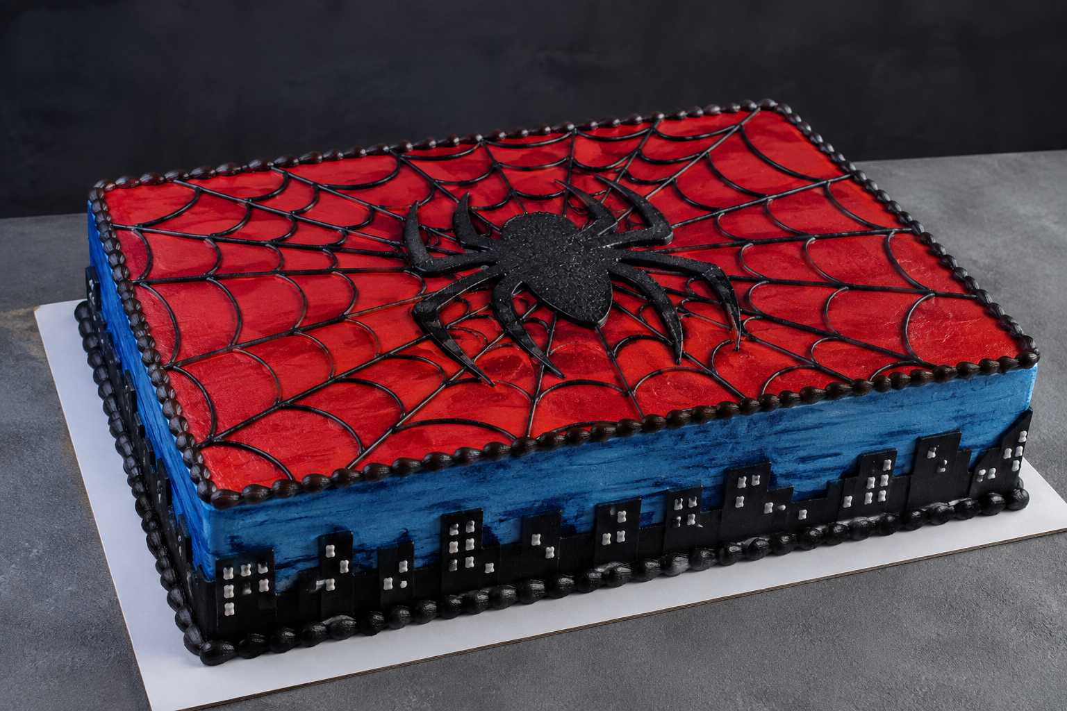 Slab cake decorated with a spider web design and a black spider on top, themed for Spider-Man, with blue and black cityscape decorations on the sides.