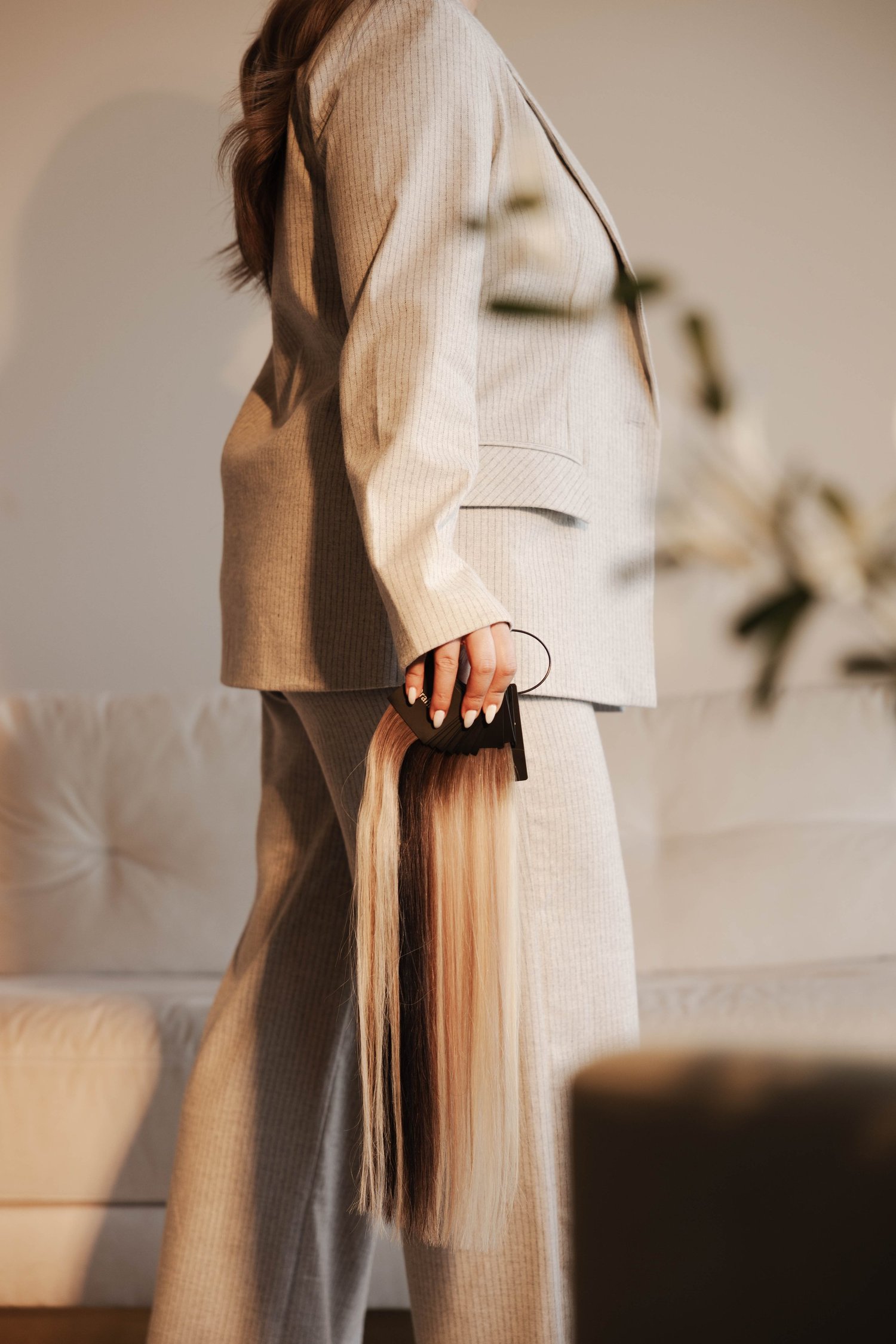 Stylist in a beige suit holding hair extensions