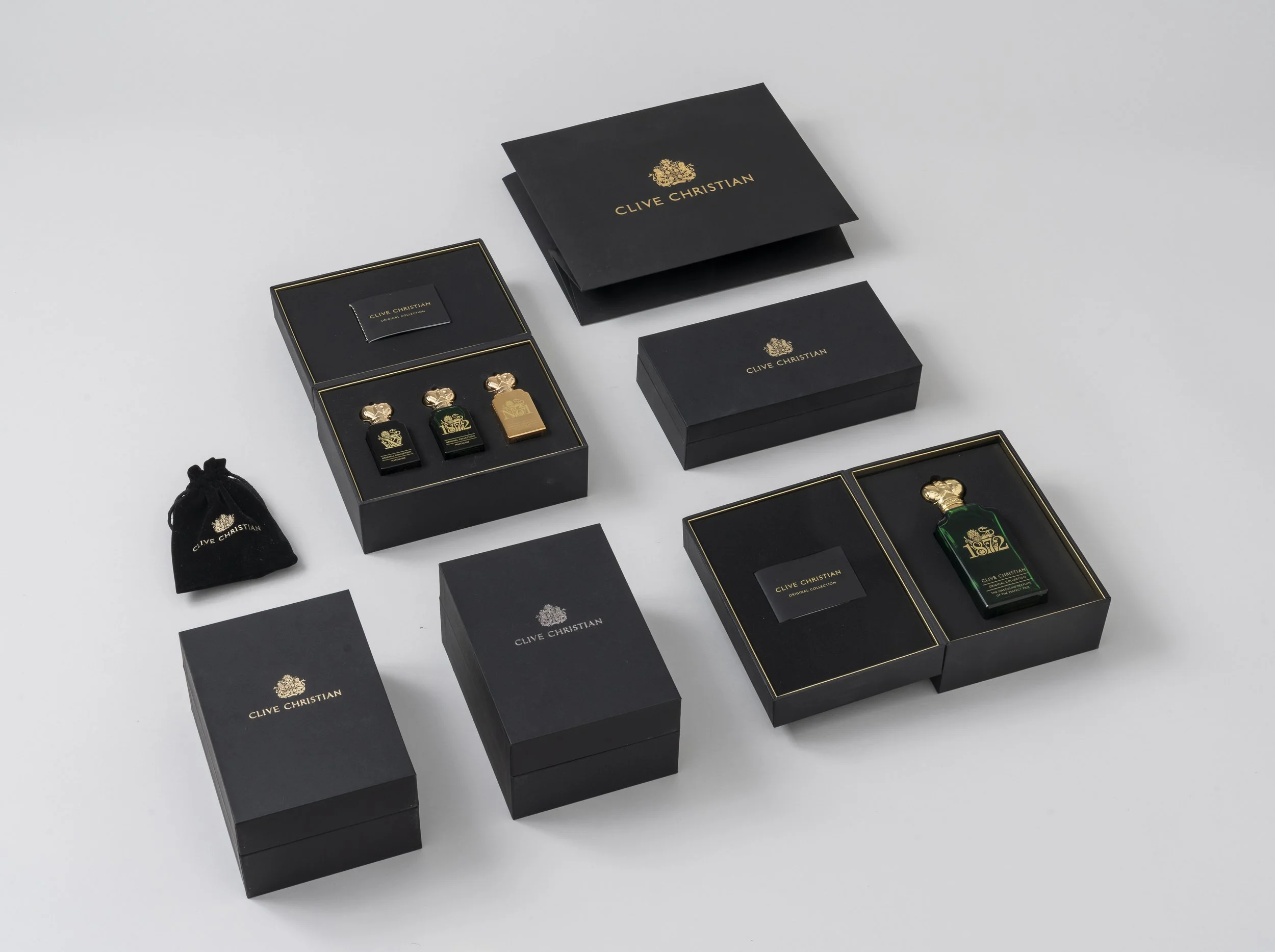 Collection of black boxes with gold accents, containing perfume bottles and accessories, with a small black drawstring pouch, all branded Clive Christian.