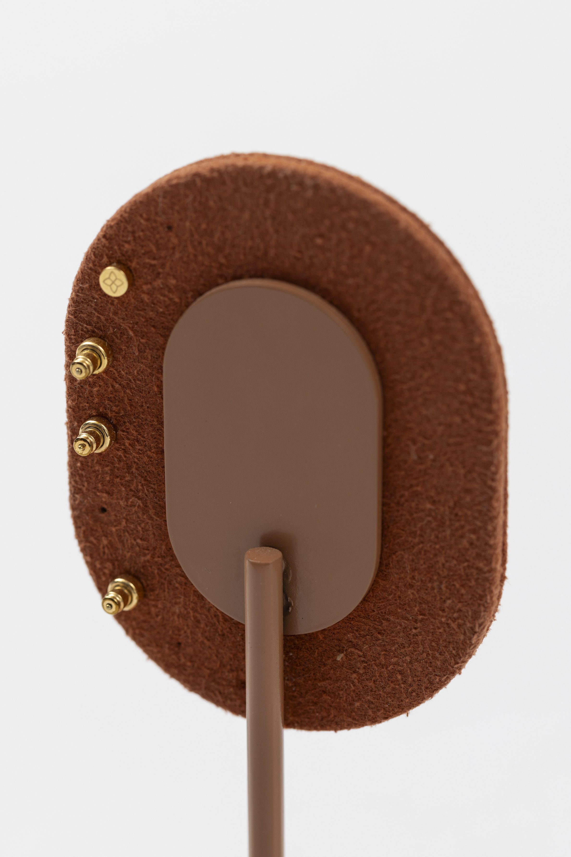 Close-up of the back of a brown and rust-colored stand or mount with a gray oval attachment and four gold screws.