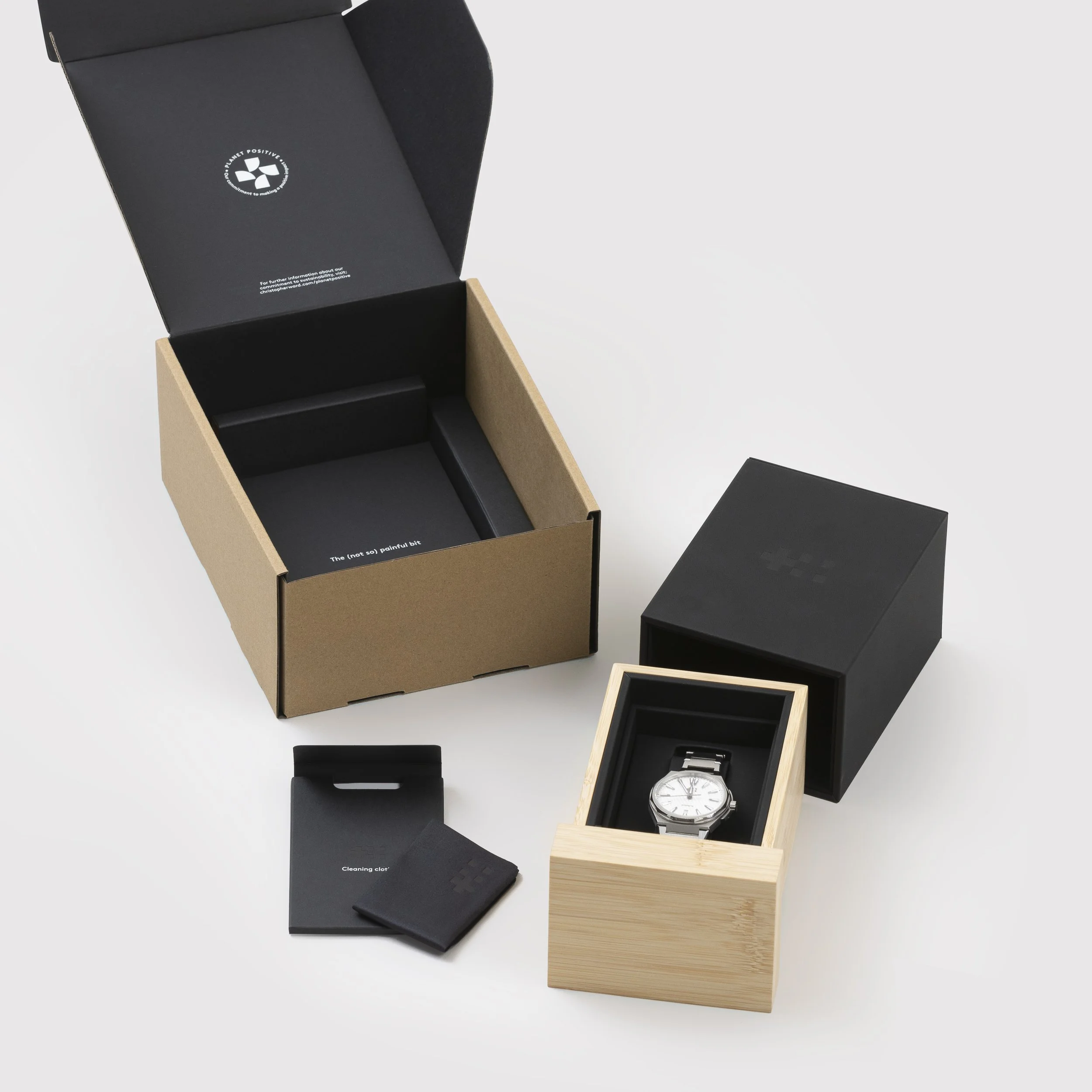 A wristwatch in a wooden box, with a black outer box and cleaning cloths, on a white surface.