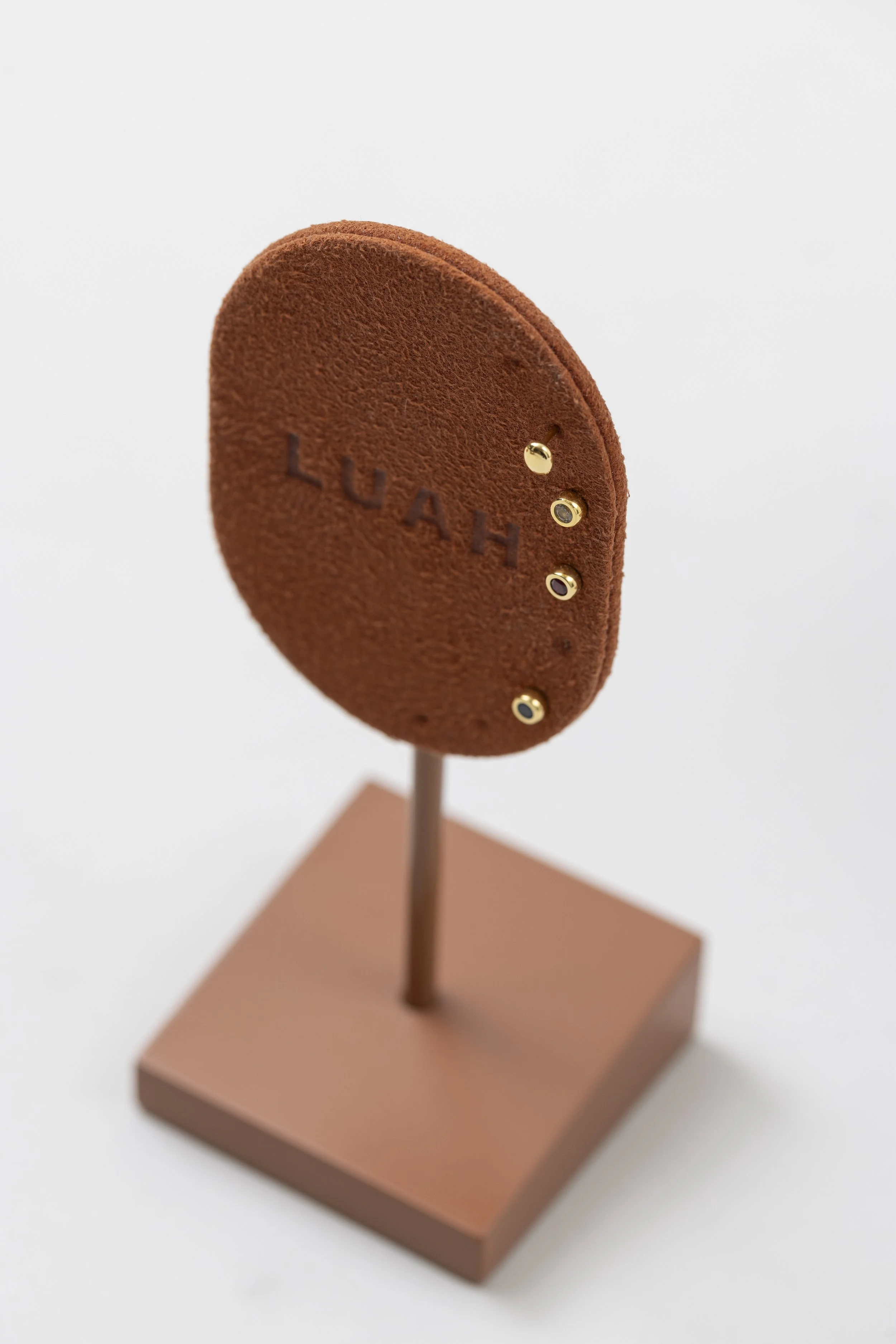 An earring display with "LUAH" debossed on it, mounted on a stand with earrings studded through it