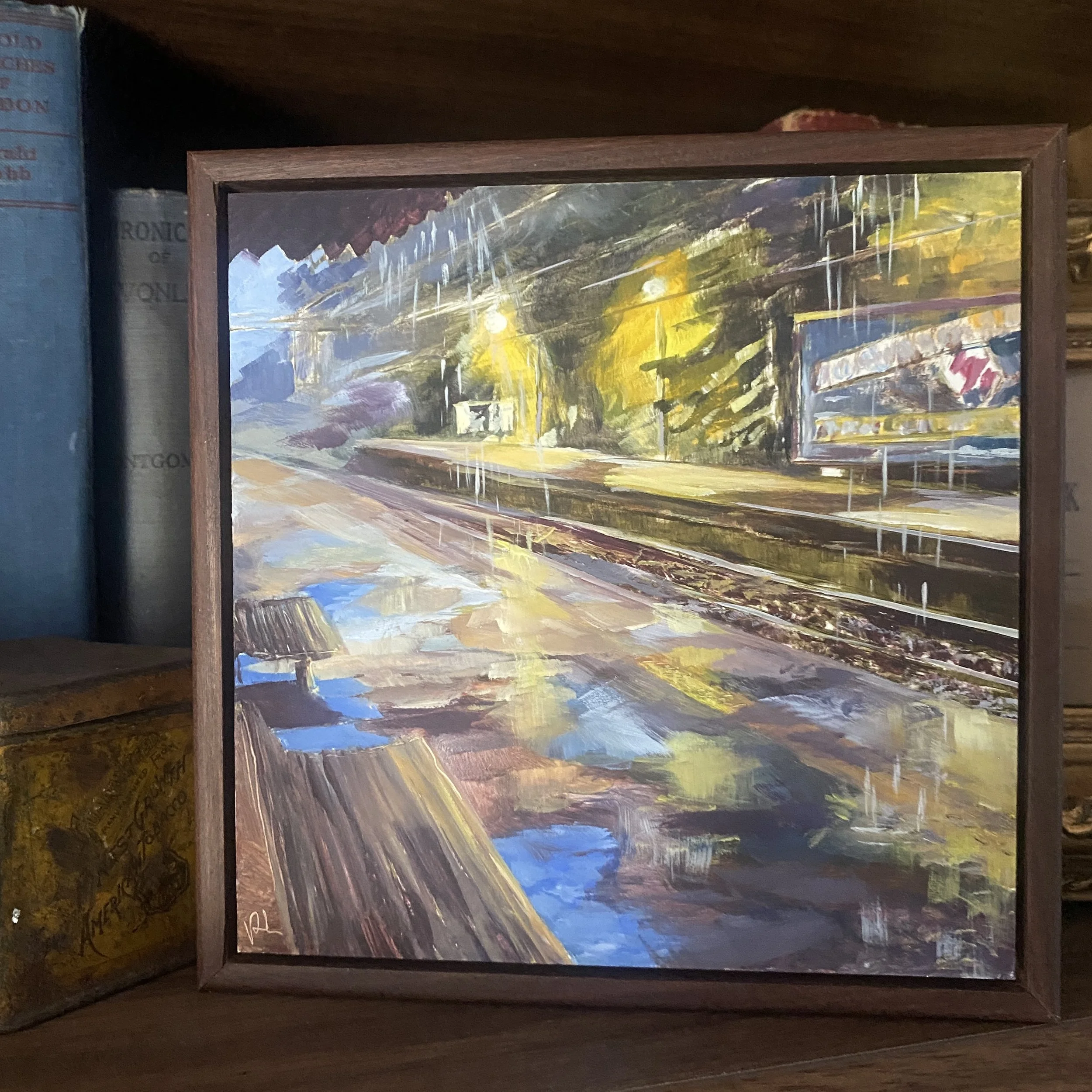 I like how it is dark and raining but the viewer in under cover and dry.  The billboard is lit up over on the other platform and the lights highlight the rain coming down.