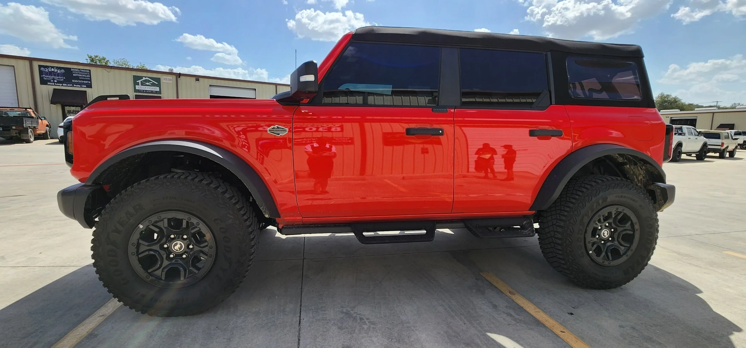 Red off-road SUV with large tires parked in a lot against a blue sky with clouds.
