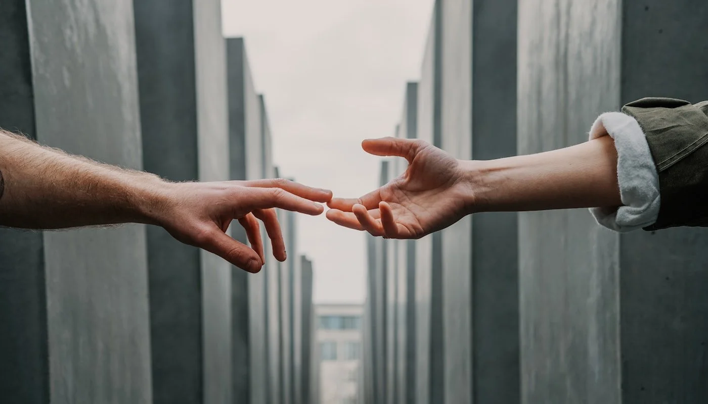 Two hands reaching out to each other between two buildings in an urban setting.
