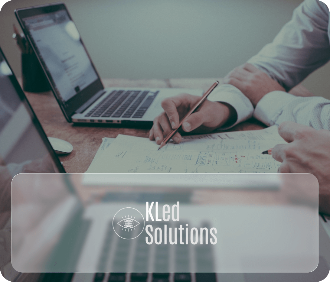 Two people reviewing documents and working on a laptop and tablet in an office setting, with a logo for KLed Solutions overlayed on the bottom.