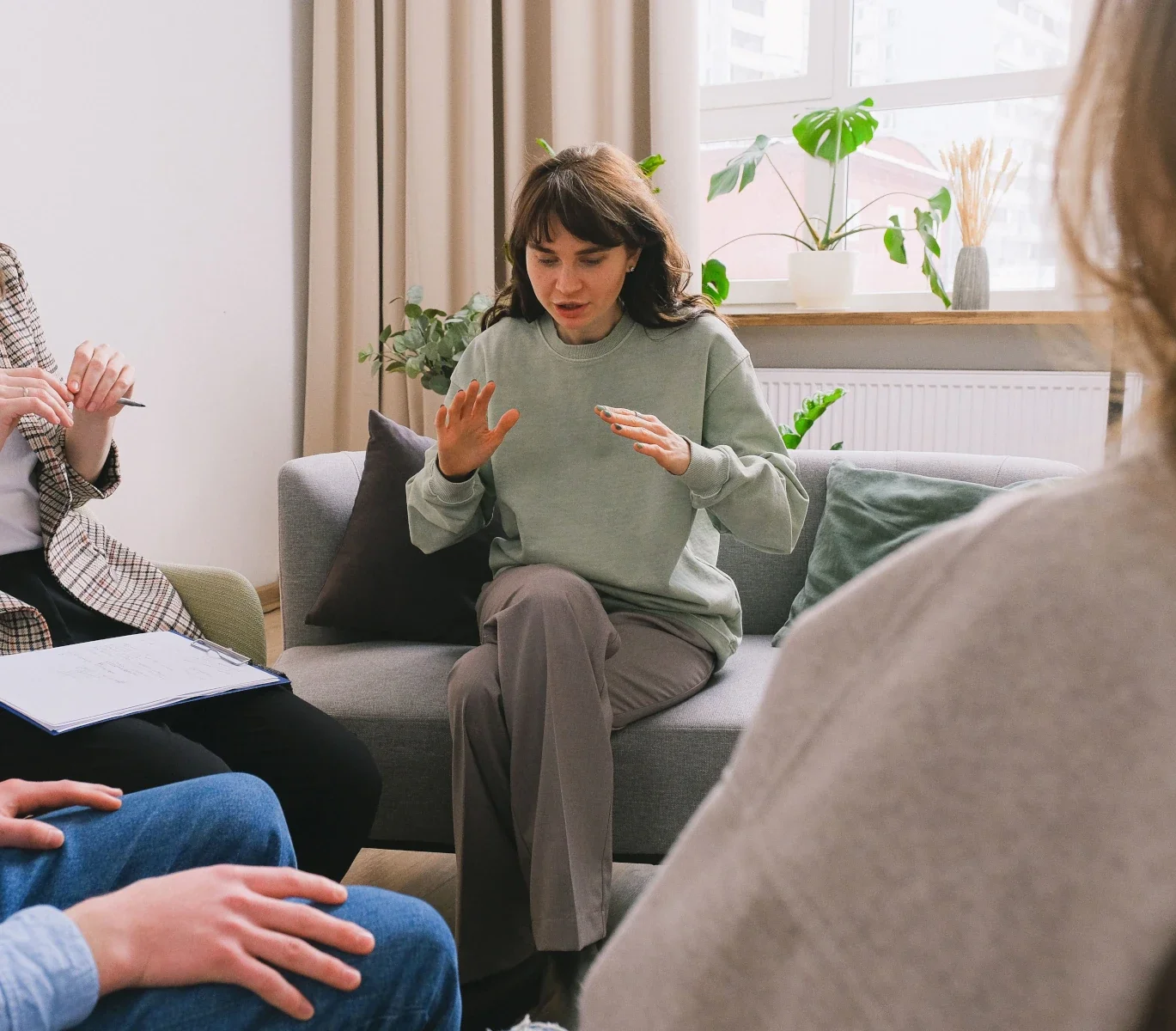 Participants sharing their experiences during a group therapy session led by a counselor holding a clipboard.