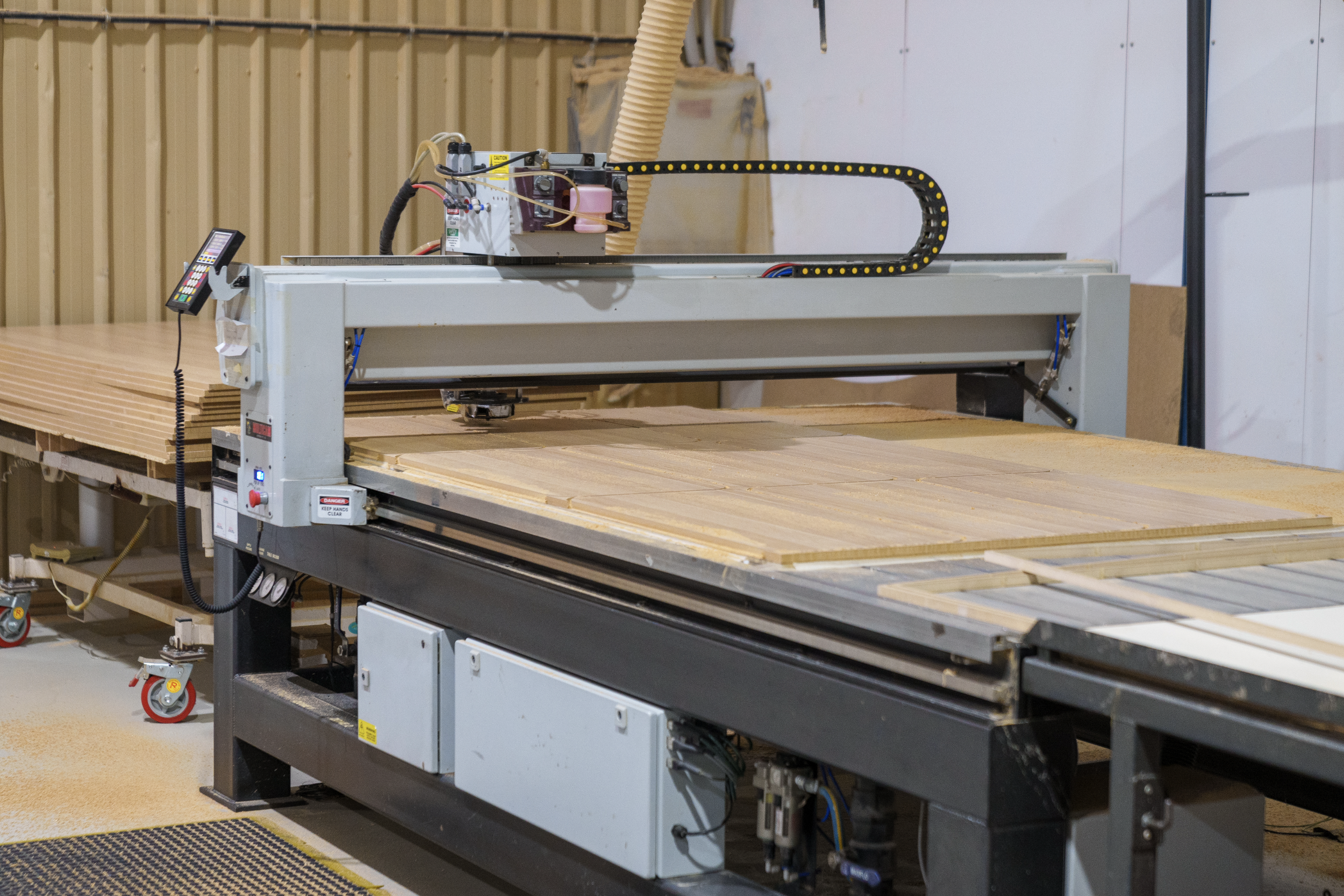 Industrial woodworking CNC machine operating on a sheet of plywood in a workshop.
