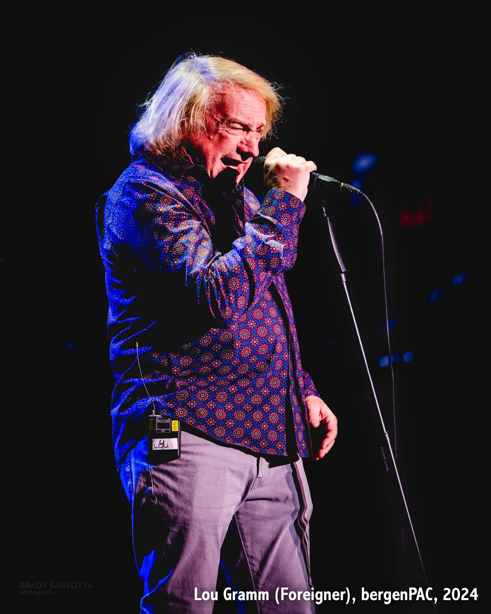 Lou Gramm of Foreigner singing under deep blue backlighting during a classic rock concert at BergenPAC in Englewood, NJ.