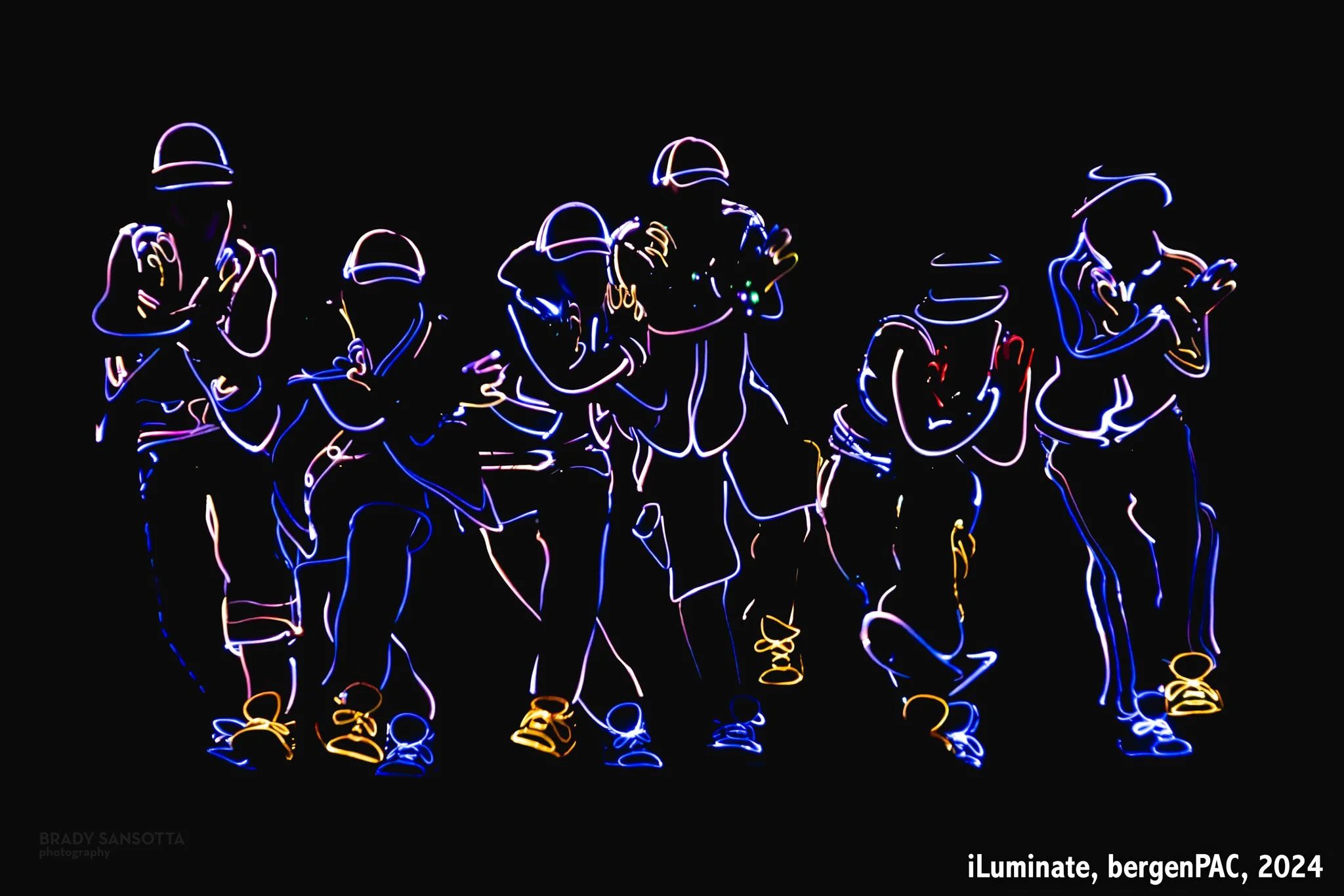 Stage photo of iLuminate dancers with lit costumes during a performance at BergenPAC in Englewood, NJ.
