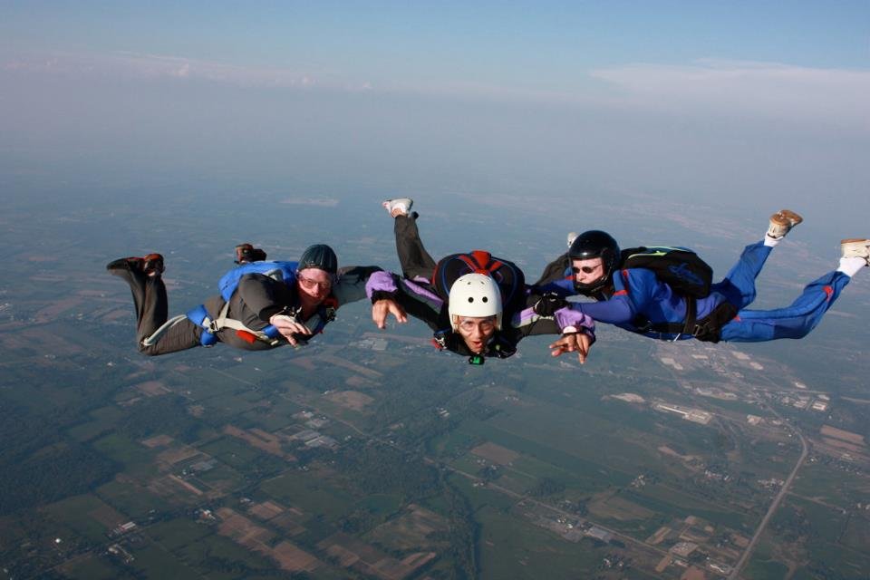Three skydivers free-falling in midair over a landscape of fields and roads.