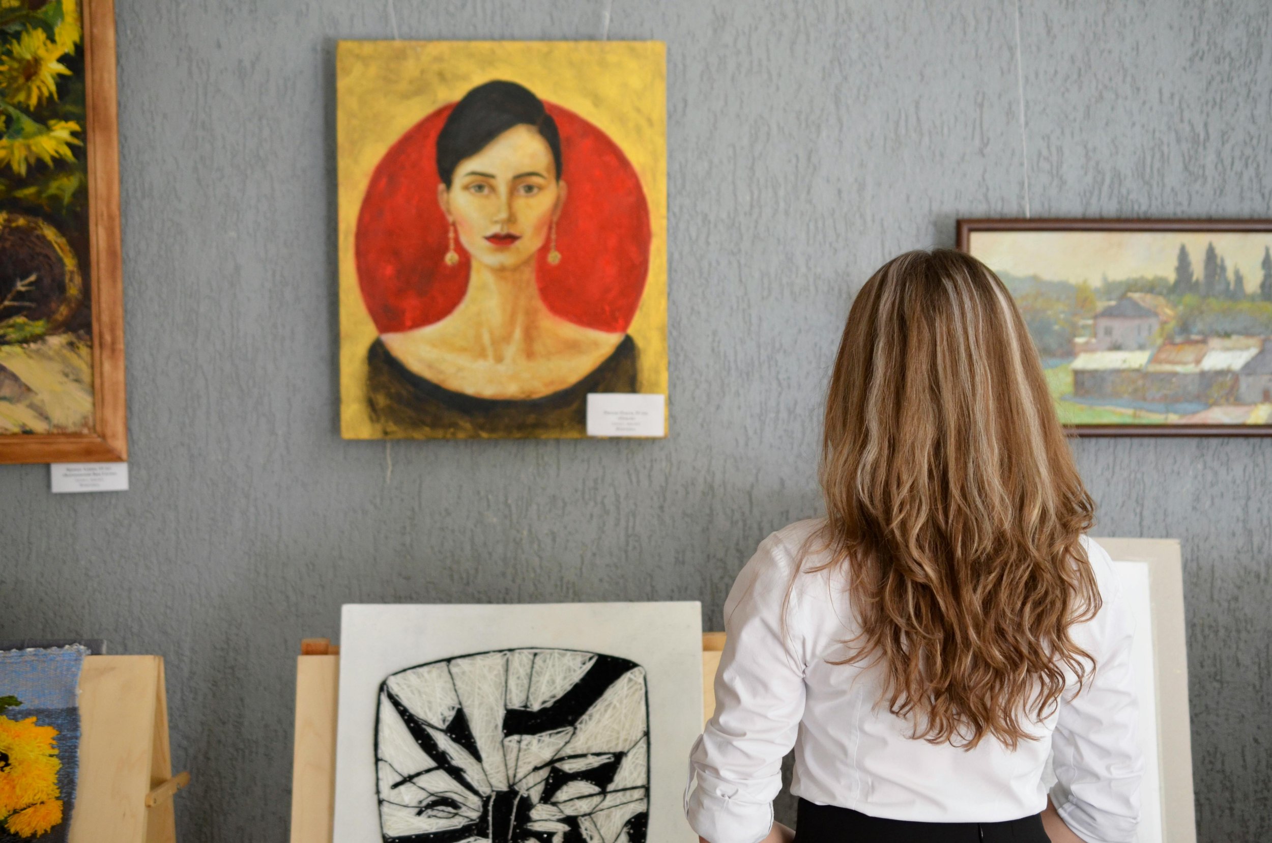 Visitor observing portrait paintings in a gallery setting with multiple artworks on display