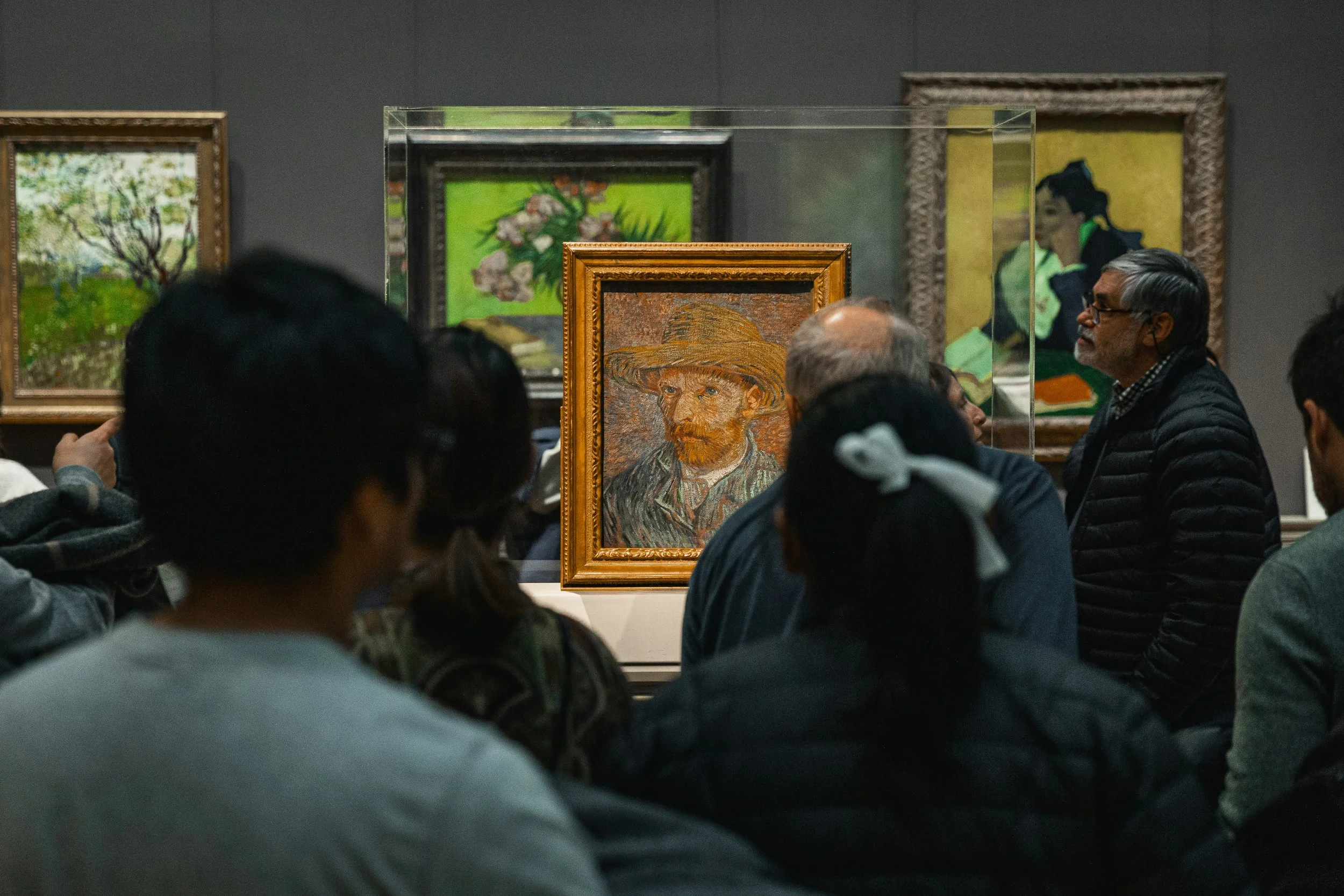 Visitors gathered around a framed painting in a museum gallery viewing an artwork on display