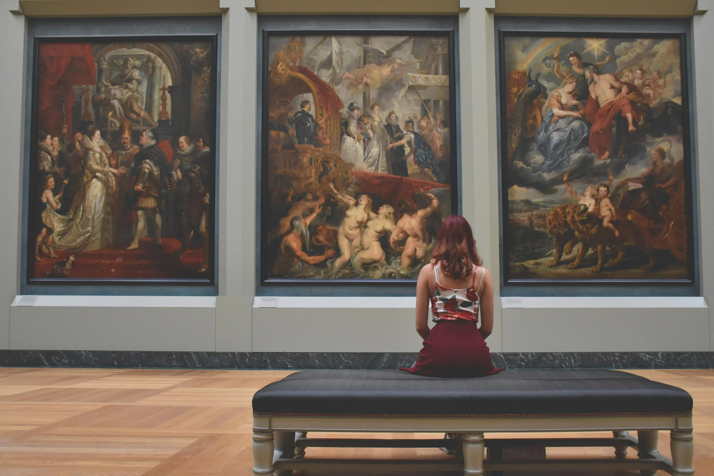 Woman seated on bench observing classical paintings in a museum gallery