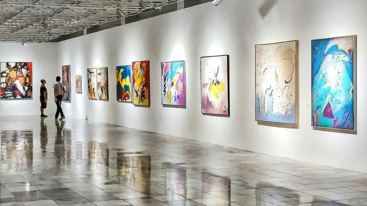 Contemporary art gallery with colourful abstract paintings displayed along a large exhibition wall