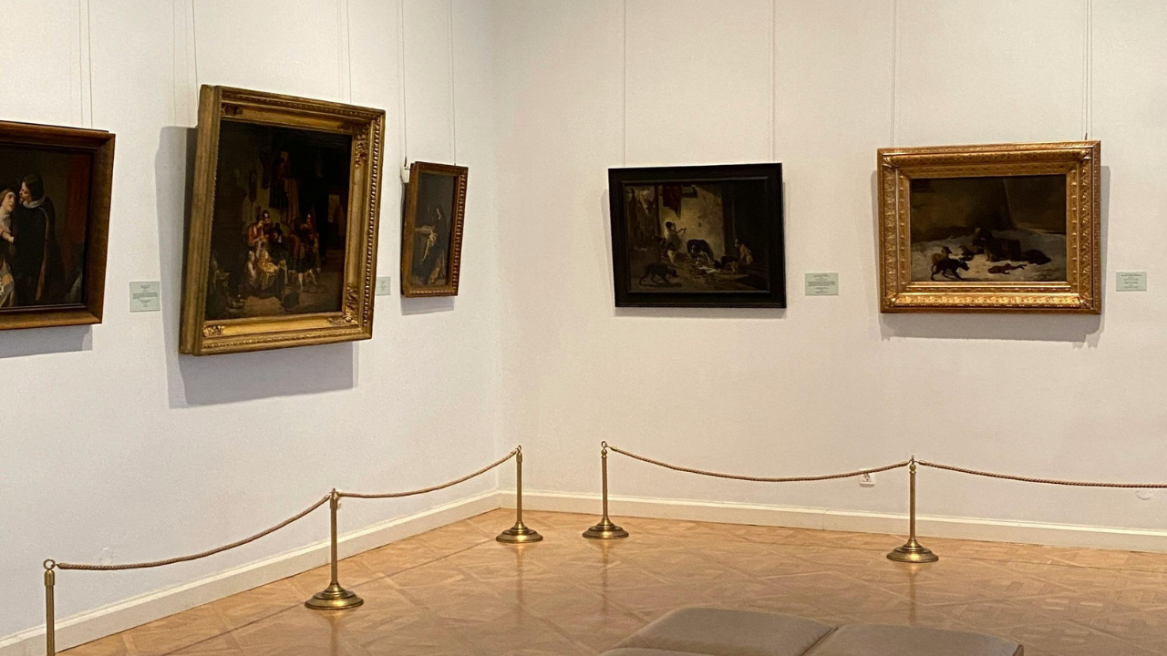 Interior of a museum gallery displaying framed classical paintings with seating in the center