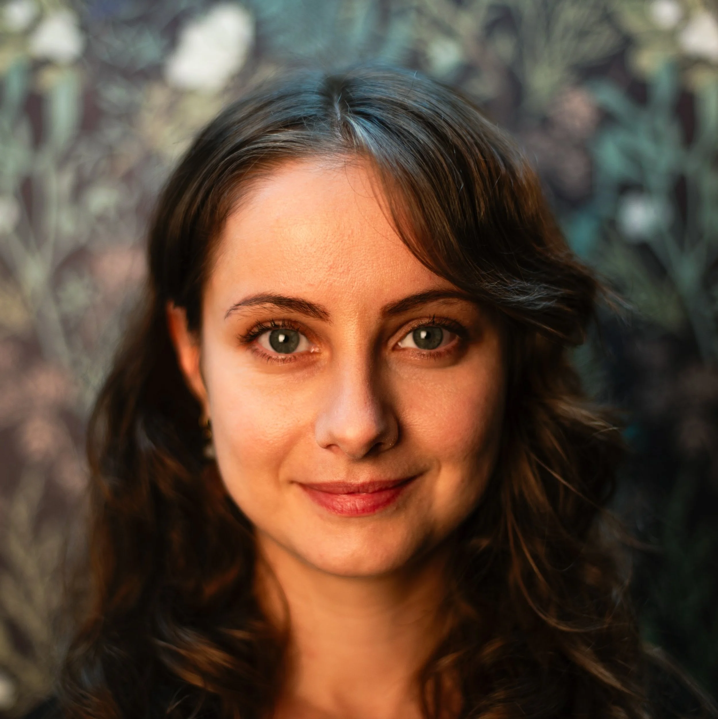A headshot photo of the woman who owns Laura Miller Osteopathy. She has long dark hair, and friendly closed mouth smile, and light skin with light hitting her face from the left side of the room.