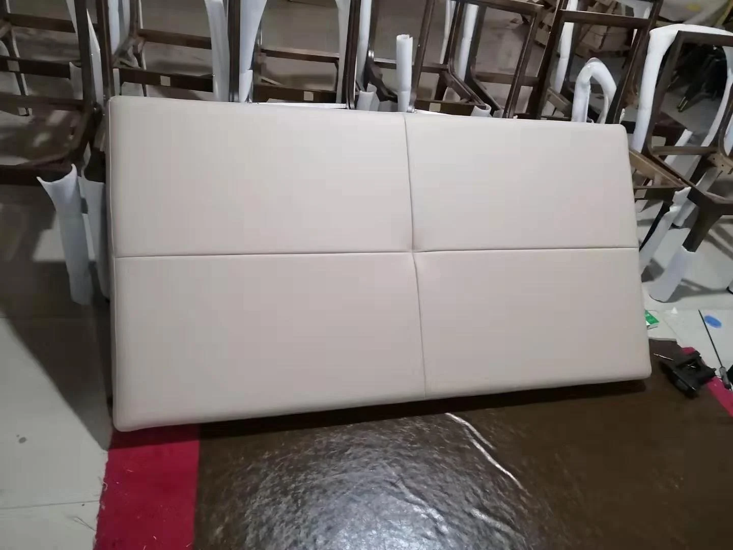 A white upholstered sofa with four sections, positioned in a warehouse or storage area surrounded by disassembled chairs and furniture.