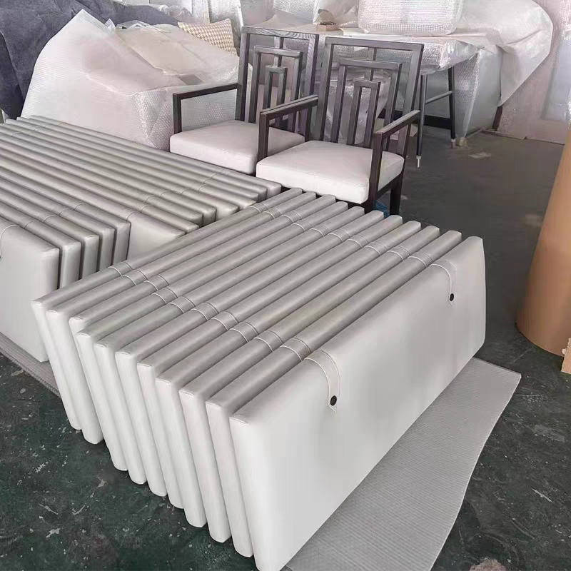 A collection of modern furniture including white upholstered stools, black wooden armchairs with white cushions, and a few other pieces stacked or covered in protective wrapping in a storage or showroom setting.