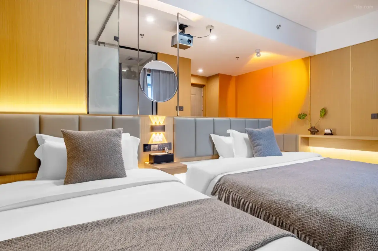 Two neatly made hotel beds with gray pillows and throws in a modern, well-lit hotel room with wooden accents and minimal decor.