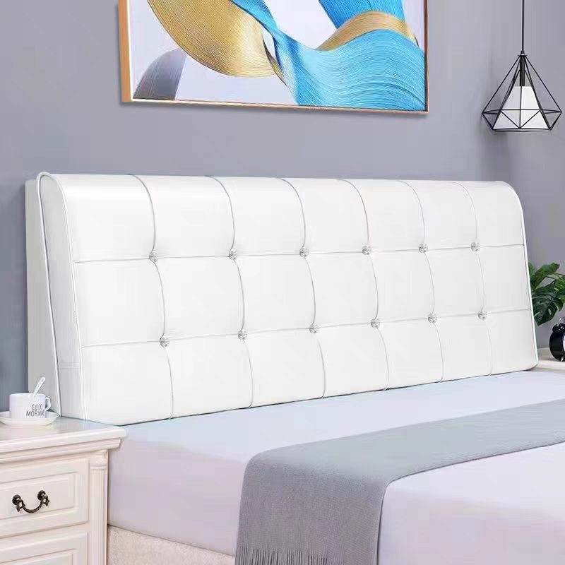 A white upholstered headboard with button tufting on a bed in a modern bedroom. There is a nightstand with a mug and spoon, a framed abstract painting, and a geometric pendant light fixture hanging from the ceiling.