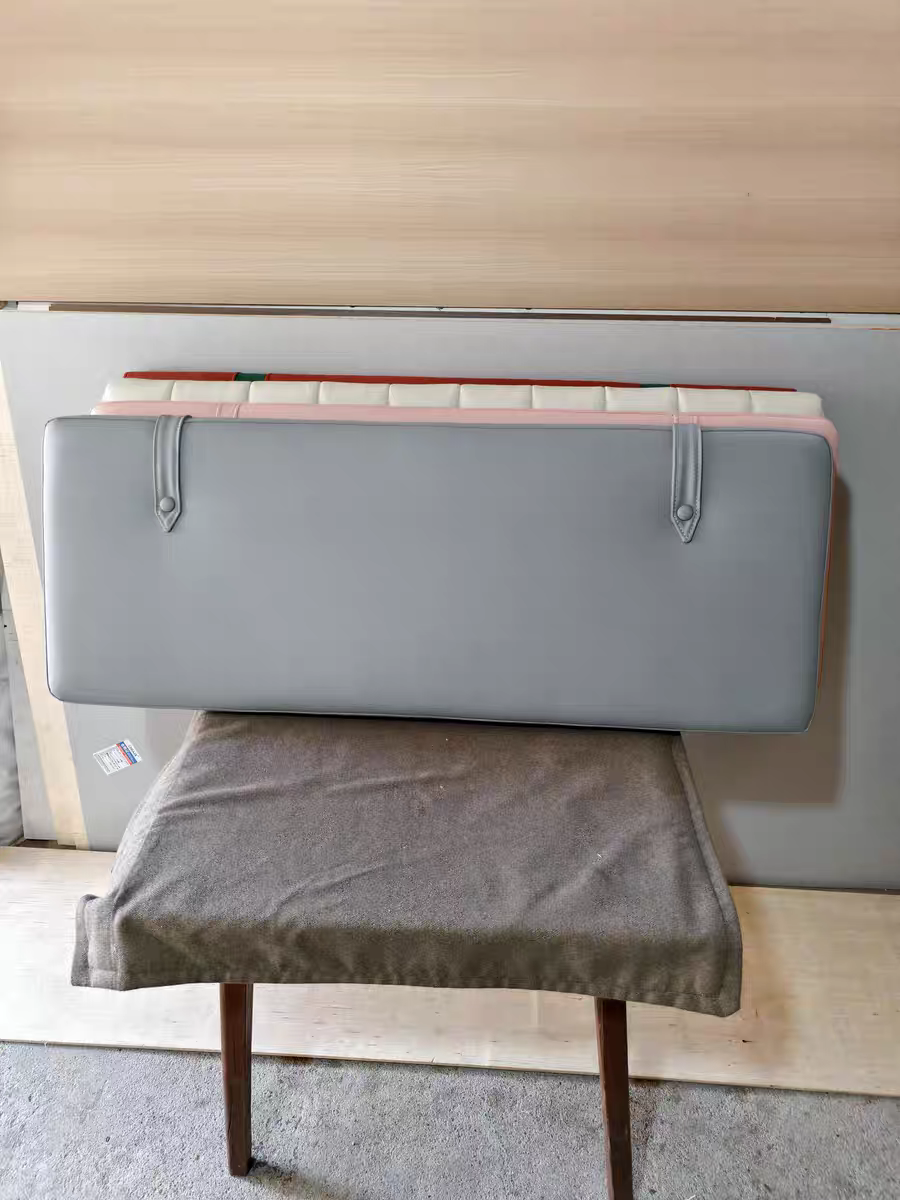 Top view of a gray seat cushion and backrest placed on a wooden chair with a fabric cover. The background includes a wood-paneled wall and some bedding or fabric.