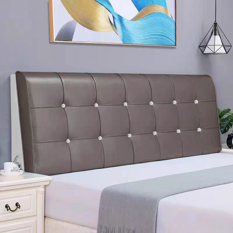 A bedroom with a modern gray upholstered headboard that has tufted buttons with diamond-like accents. There is a white nightstand on the left with a mug and spoon, and a black vase and green plant on the right. An abstract colorful painting hangs on 