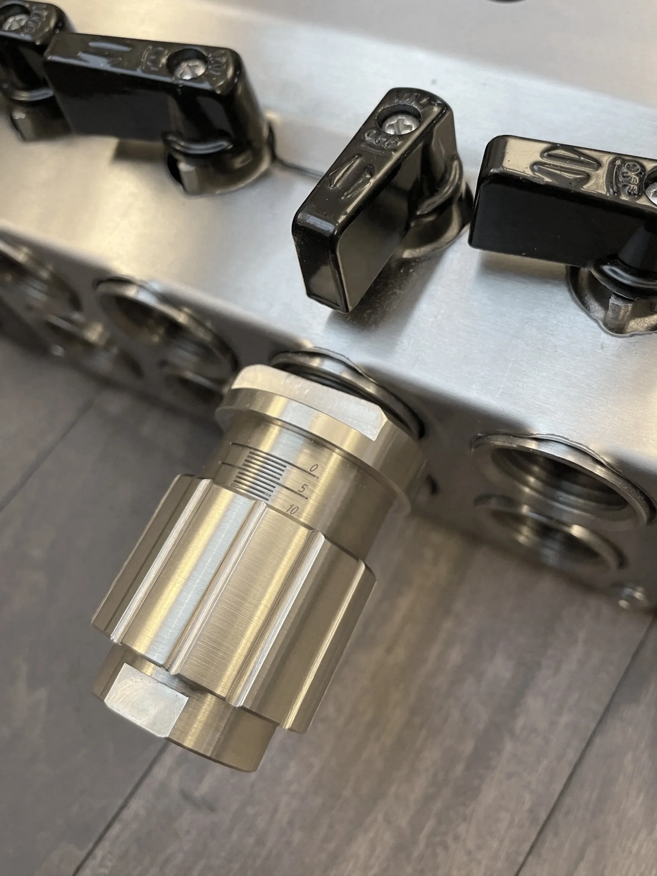 Close-up of a CNC machine or industrial equipment with a metal dial gauge and black adjustment levers.