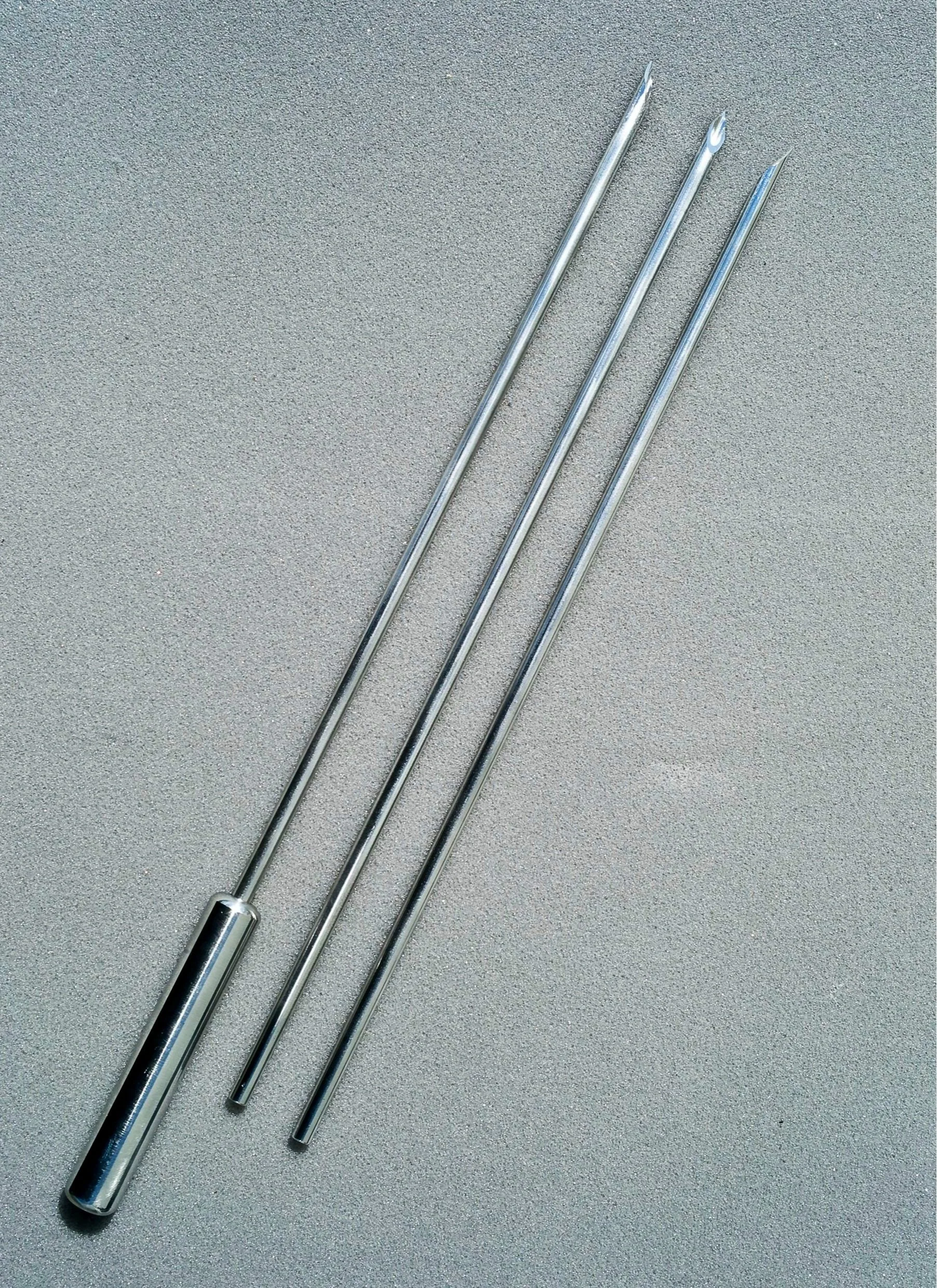 A set of four long, thin metal tools, two with pointed tips and a hollow metal tube at one end, resting on a textured gray surface.