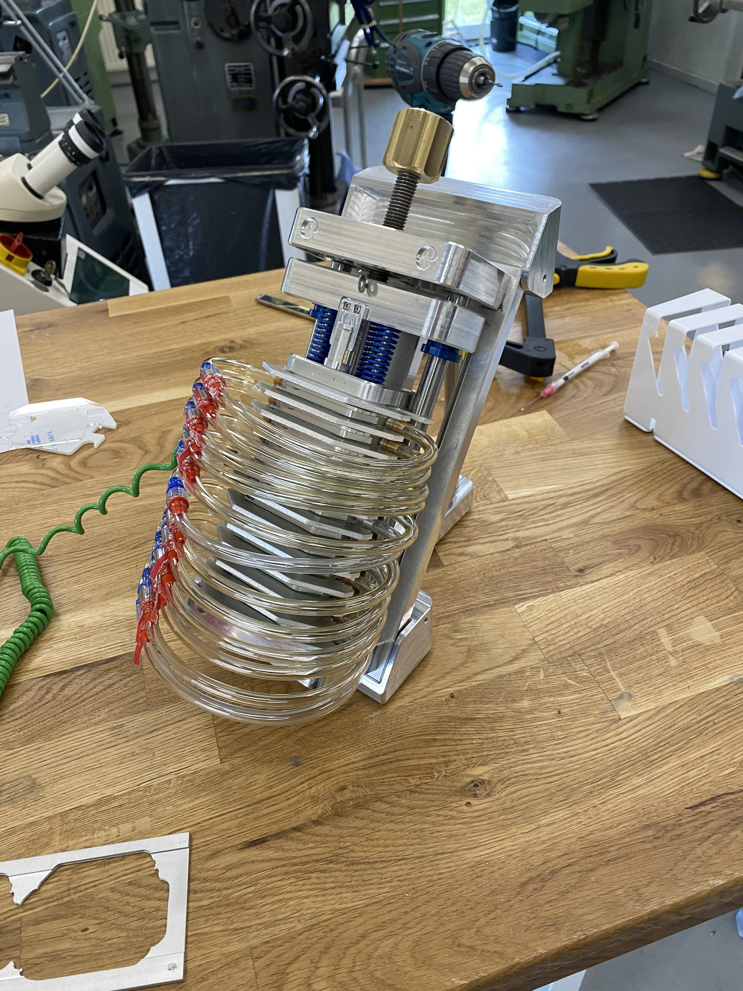 A soldering or assembly jig holding multiple circular glass or plastic disks on a wooden workbench in a workshop or laboratory setting.