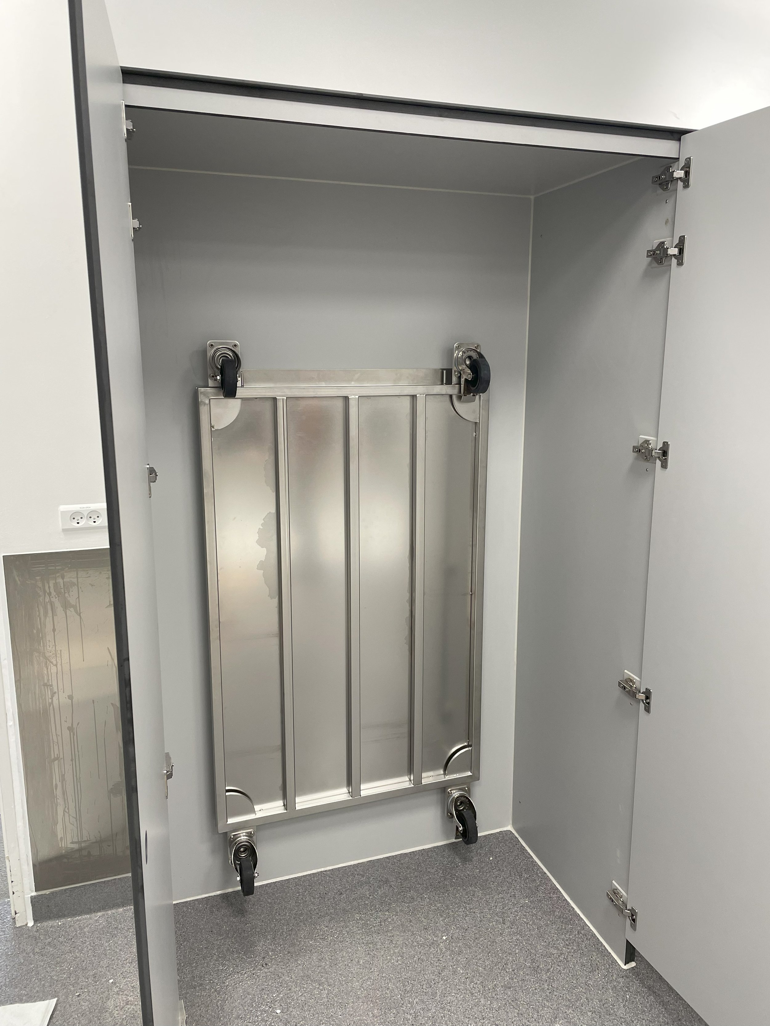 Inside a gray locker with a wheeled platform stored vertically at the back. for pharma