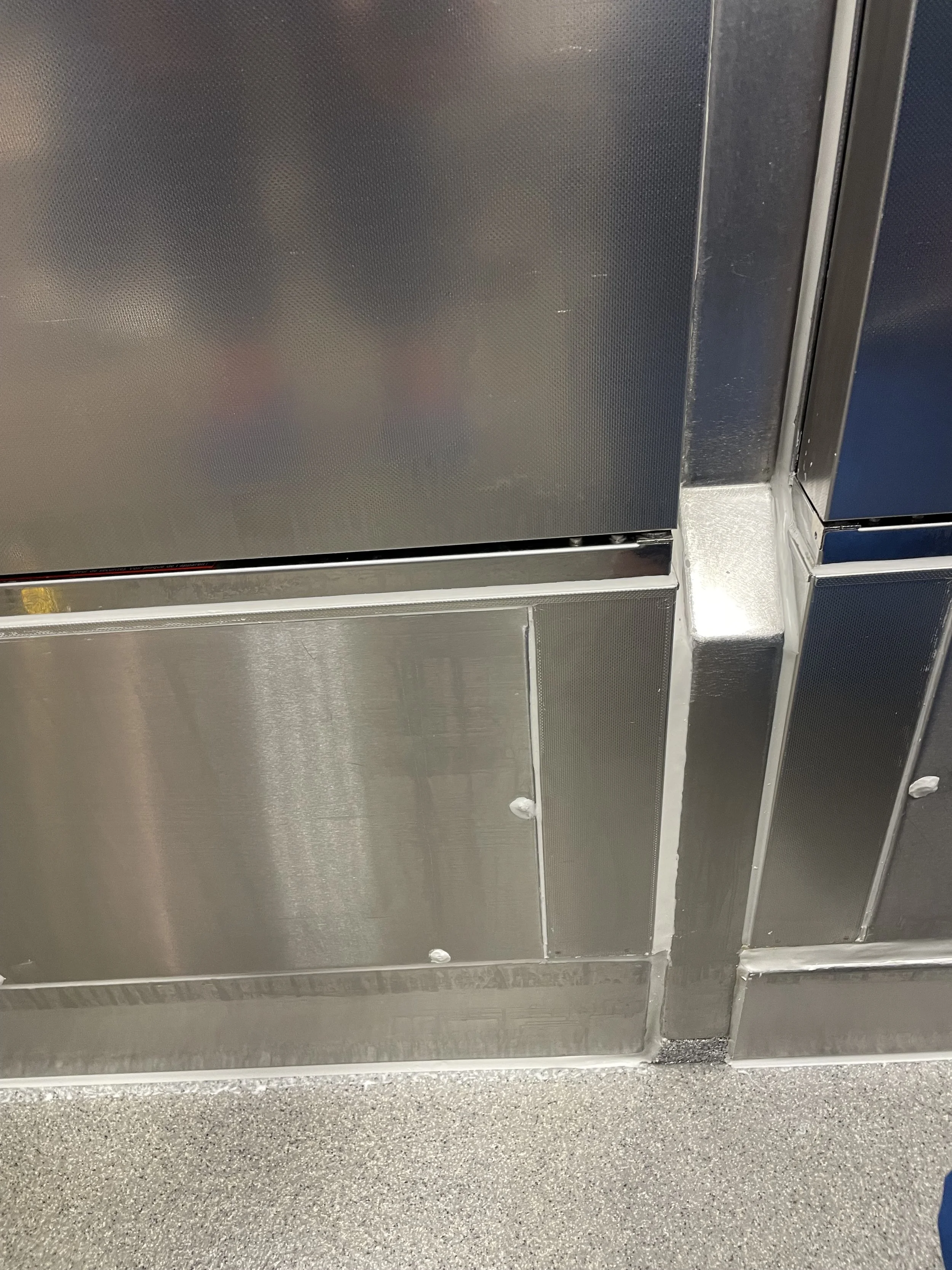 Close-up of a stainless steel kitchen appliance, likely an oven or microwave, with visible seams and screw details, and a gray textured countertop below.