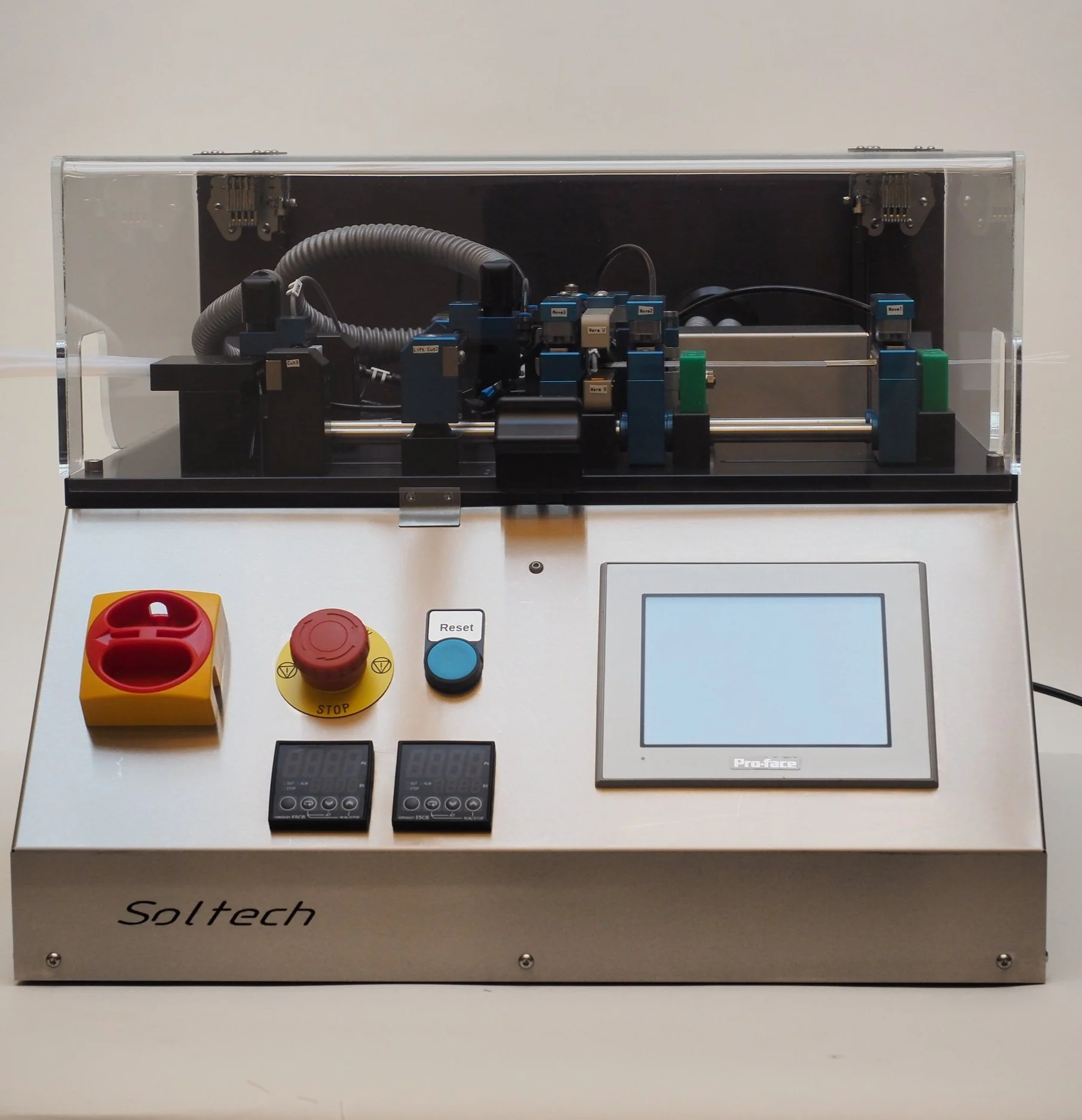A scientific or industrial machine with a transparent cover, control buttons including an emergency stop, a digital display, and two digital controllers, branded Soltech, used for automated mechanical or robotic testing.