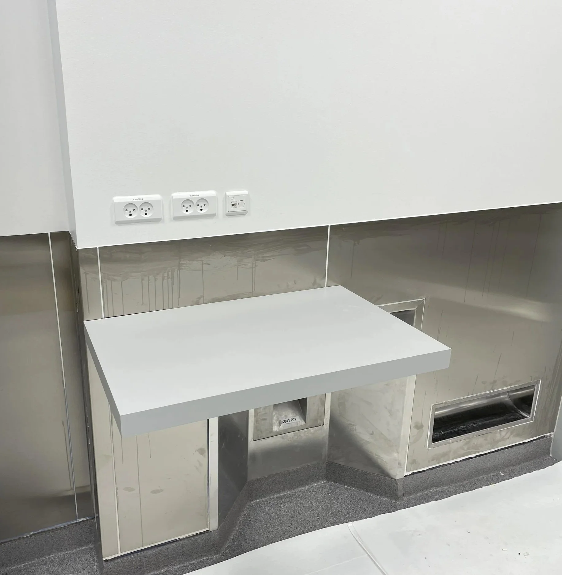 A minimalist countertop in a modern room with wall outlets, a gray wall, and metallic wall panels. for pharma