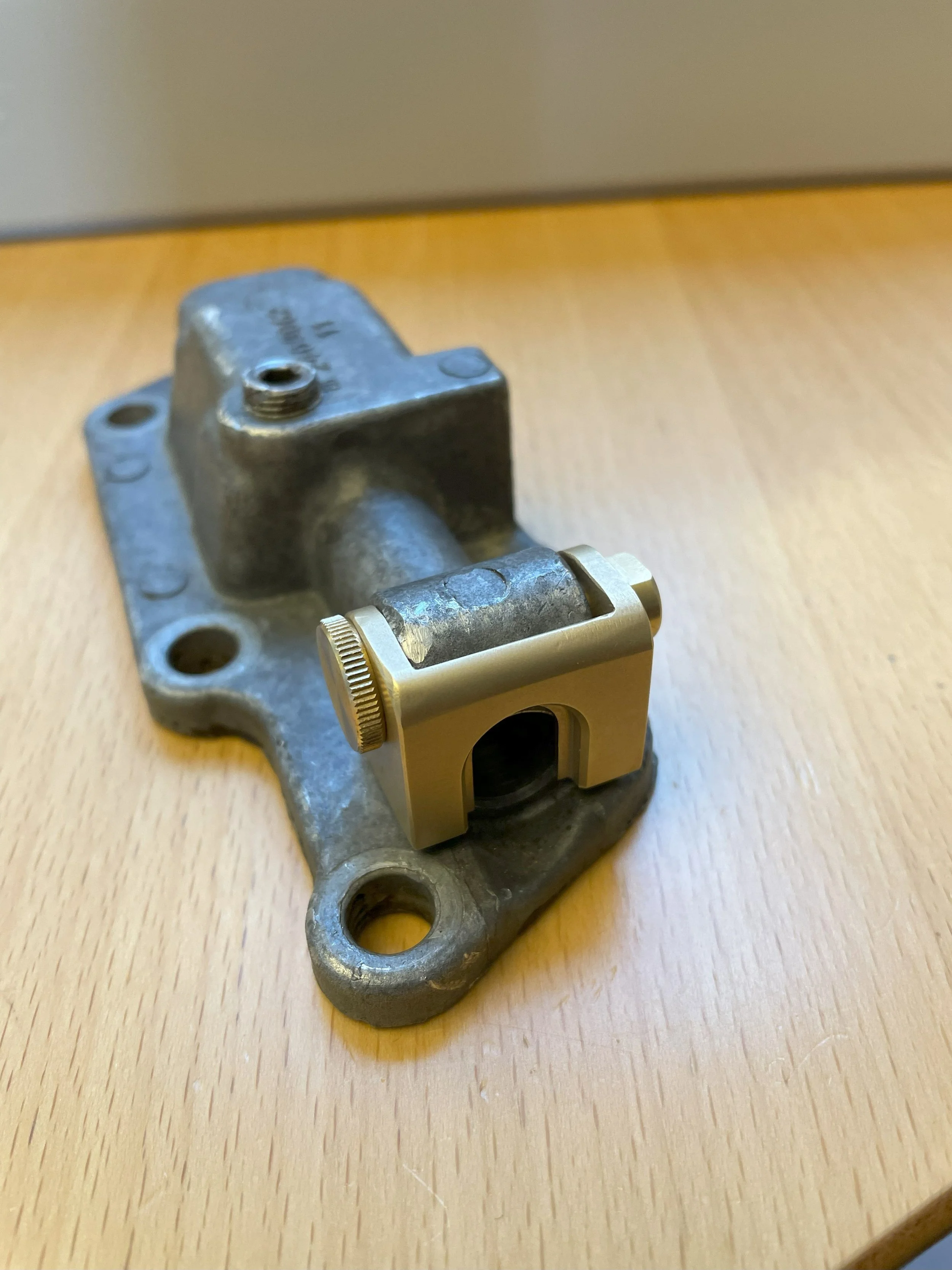 A metallic mechanical component with a mount and an adjustable brass-colored clamp, resting on a wooden surface.