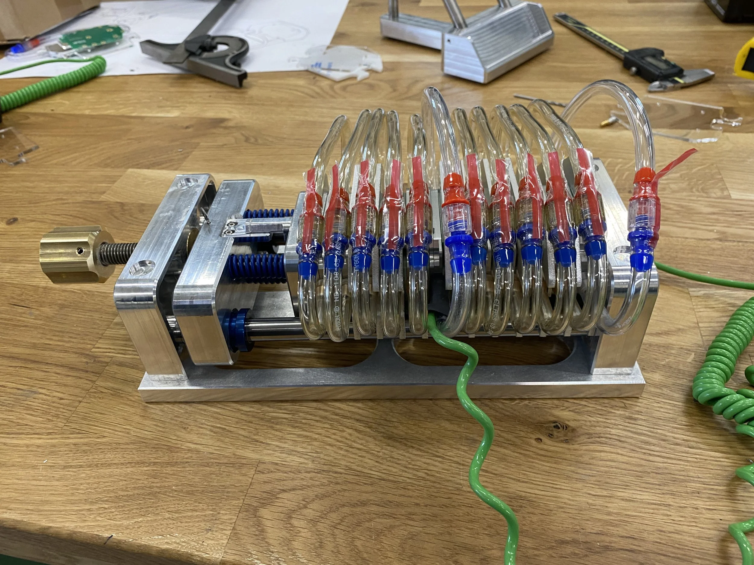 A scientific apparatus with glass tubes connected by red and blue connectors, mounted on a metal frame on a wooden workbench.