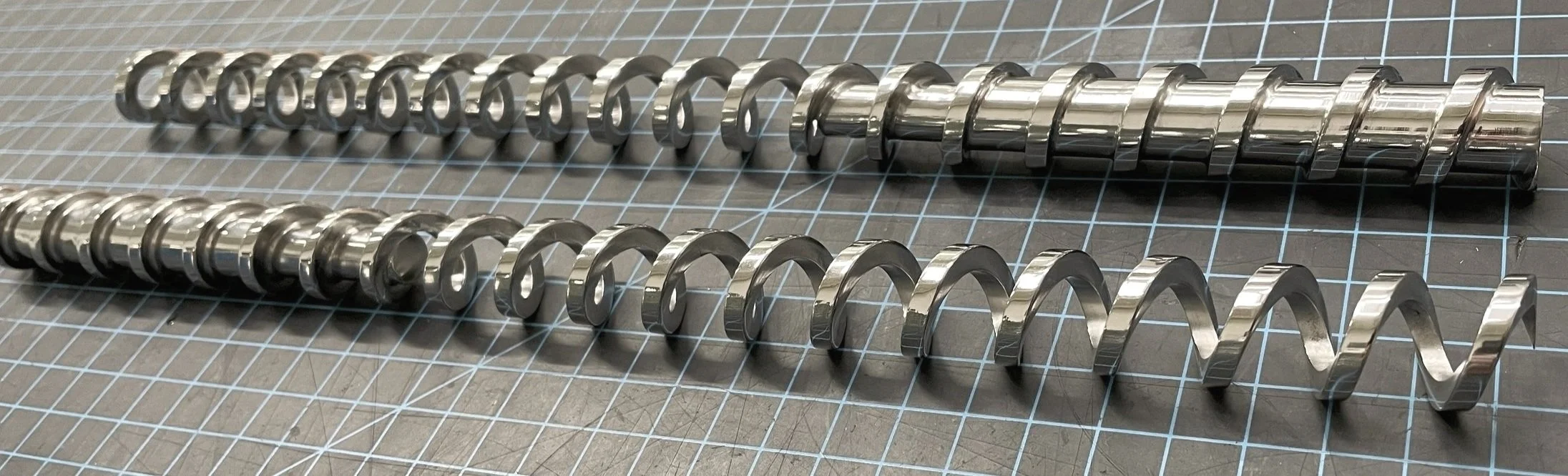 Two metal corkscrews with spiral shapes lying on a gray cutting mat with white grid lines. for pharma