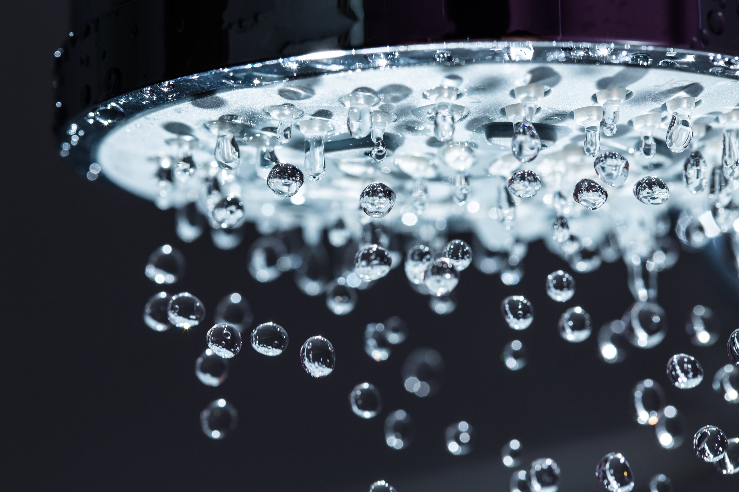 Close-up of a showerhead with water droplets falling from it.