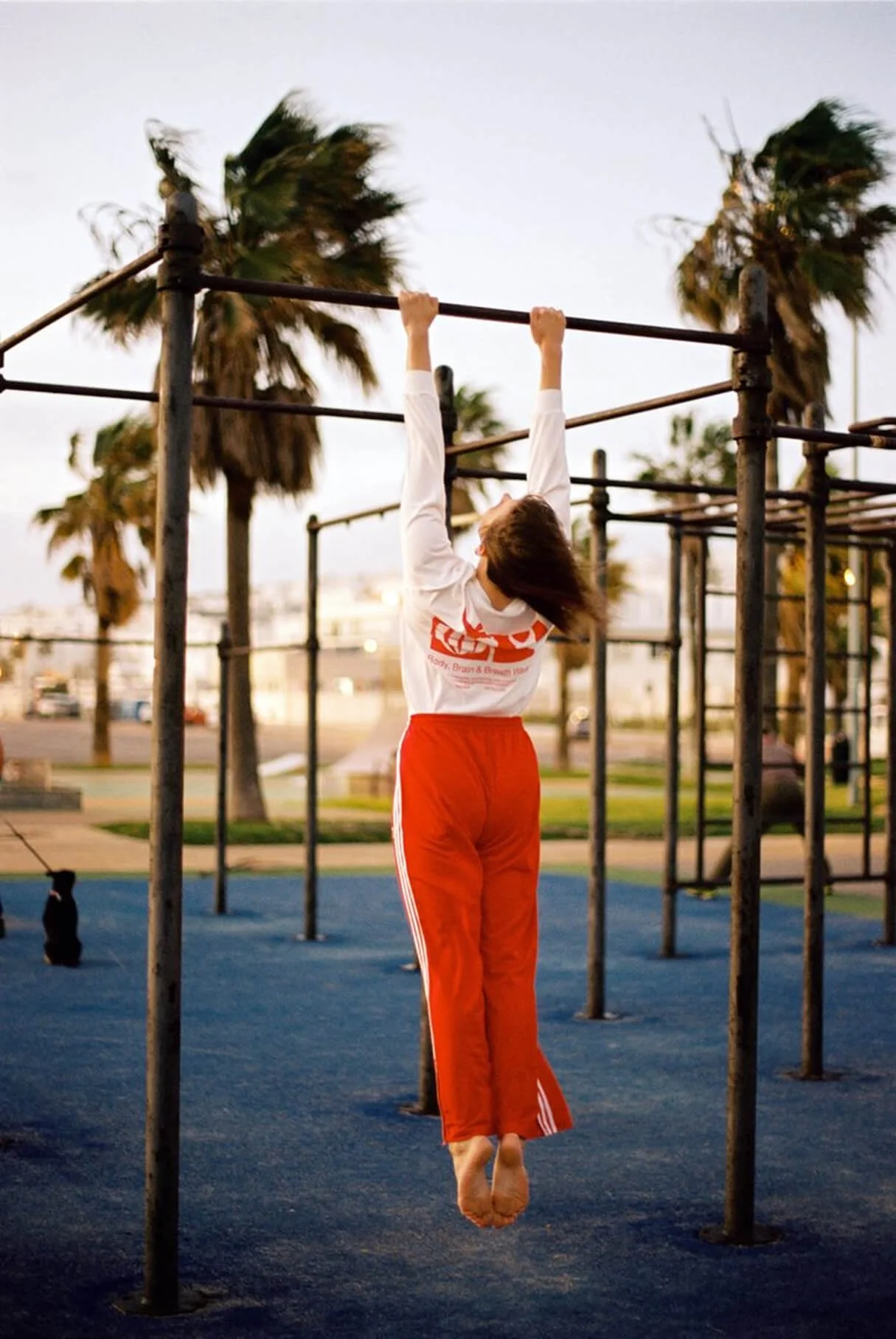 Frau hängt an einer horizontalen Stange bei Sonnenuntergang, umgeben von Palmen, auf einem Outdoor-Fitnesspark