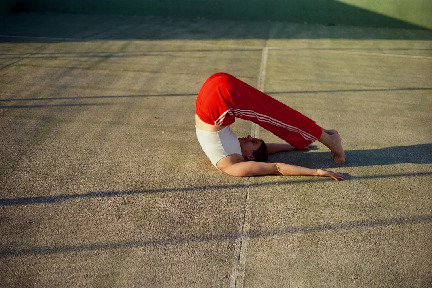 Person, die den Schulterstand im Yoga auf einer Outdoor-Sportfläche macht, mit Sonnenlicht und Schatten im Hintergrund.