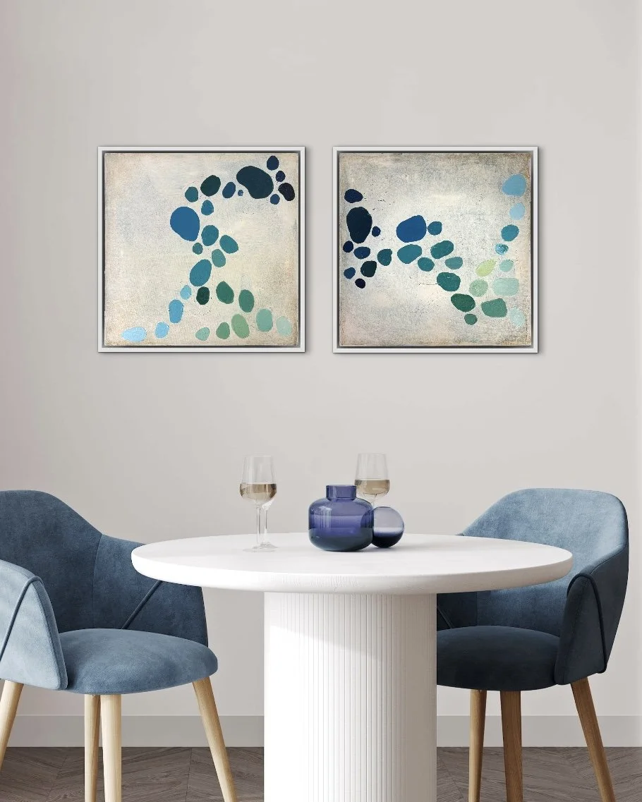 Zwei abstrakte Kunstwerke der österreichischen Malerin Birgit Trofer aus der Serie Dancing Palette, inspiriert von der Leichtigkeit im Leben, an der Wand eines Esszimmers mit weißem Tisch und modernen, samtenen hochwertigen dunkelblauen Stühlen.