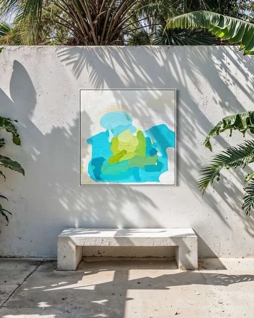 Large abstract ocean painting Shoreline Serenity by Birgit Trofer on a modern outdoor concrete wall with a bench, palm trees, and bright natural sunlight.