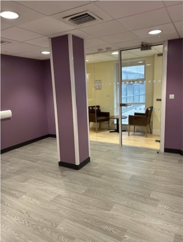  Image of the empty hub during the transformation once the floors, walls and fittings were completed. The space has deep purple walls and light wood flooring with glass doors to the corridor and a pillar at the centre of the room.  
