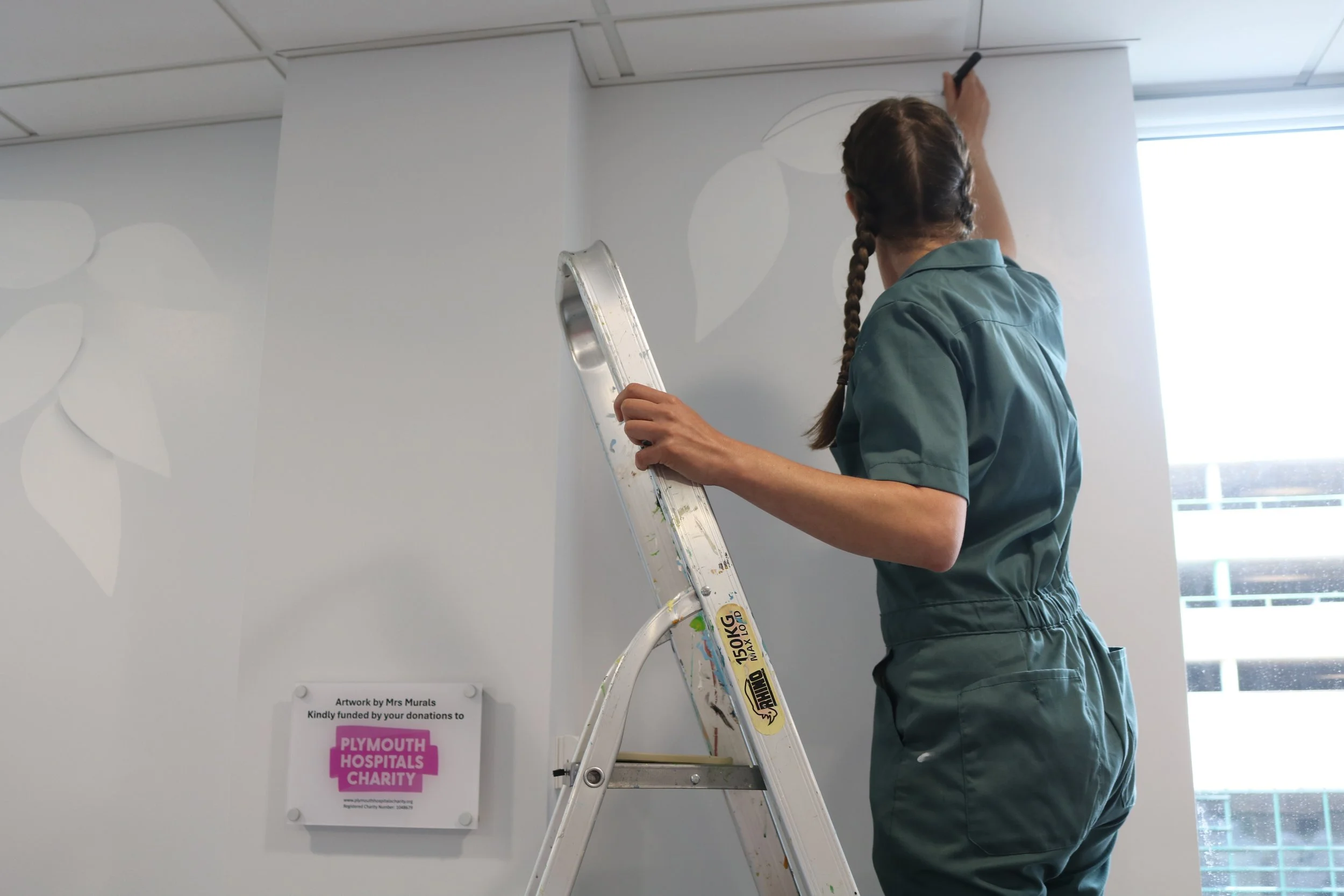 Picture of Ellie (Mrs Murals) painting the wall while on a ladder.